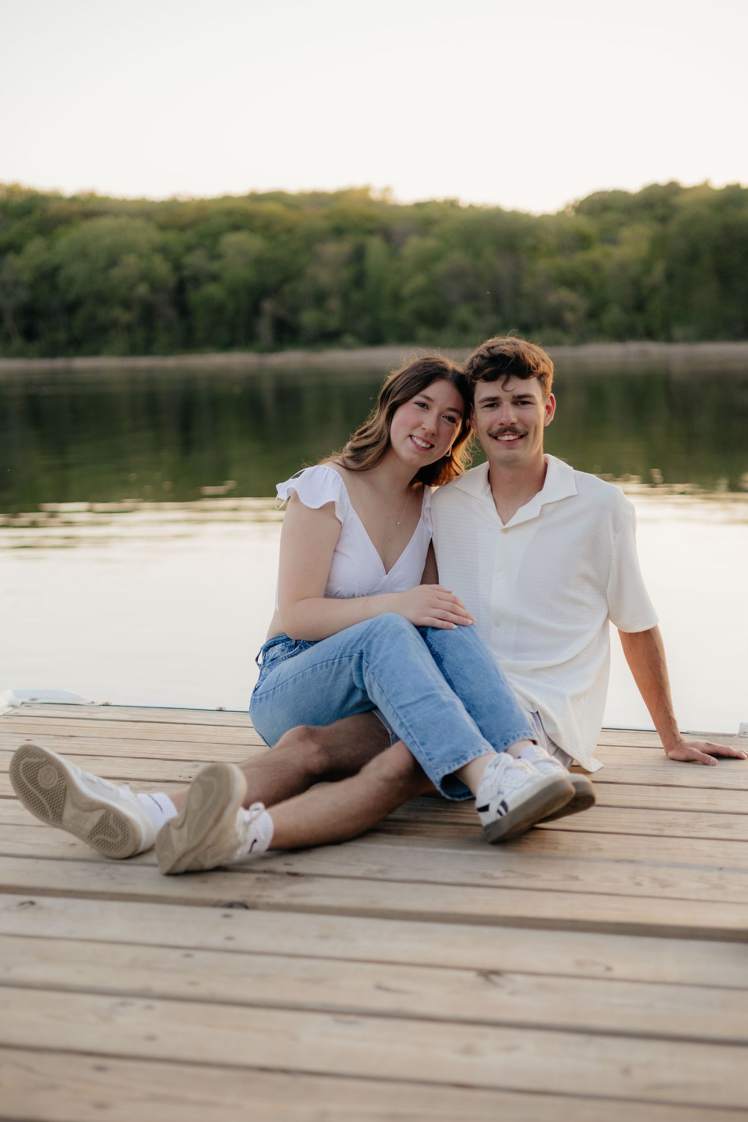 Couple smiling together along the lakeshore at Fish Lake Regional Park in Maple Grove, MN, with bright green trees and clear blue water