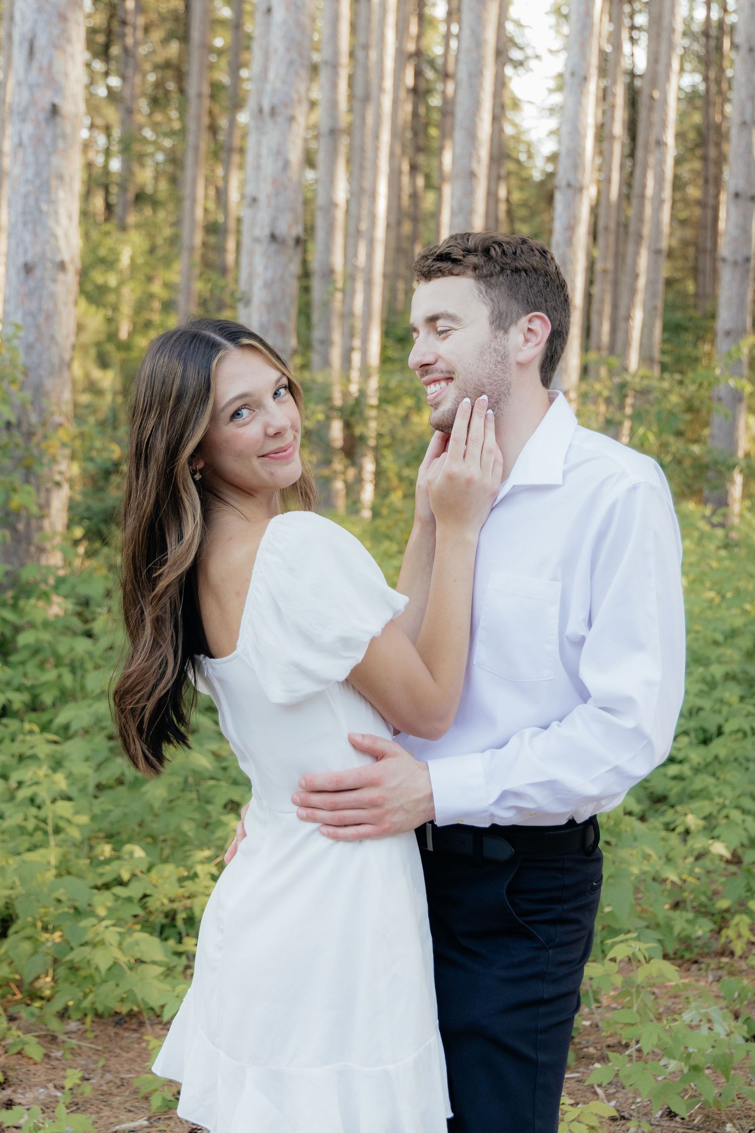Golden-hour portrait of a couple embracing among tall trees at Pinewood in Cambridge, showcasing woodsy elegance.