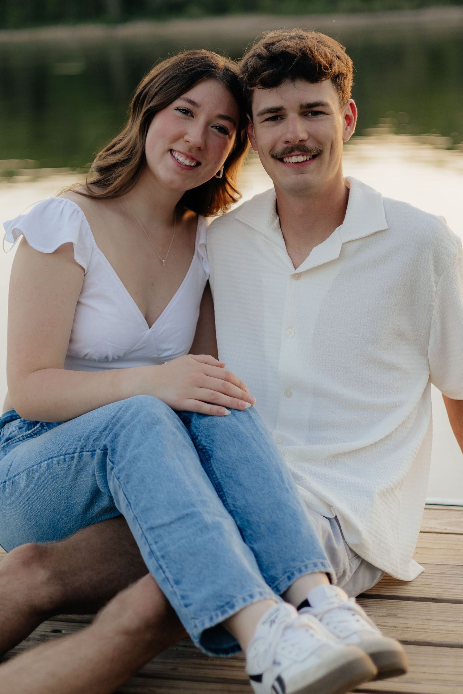 Couple smiling together along the lakeshore at Fish Lake Regional Park in Maple Grove, MN, with bright green trees and clear blue water