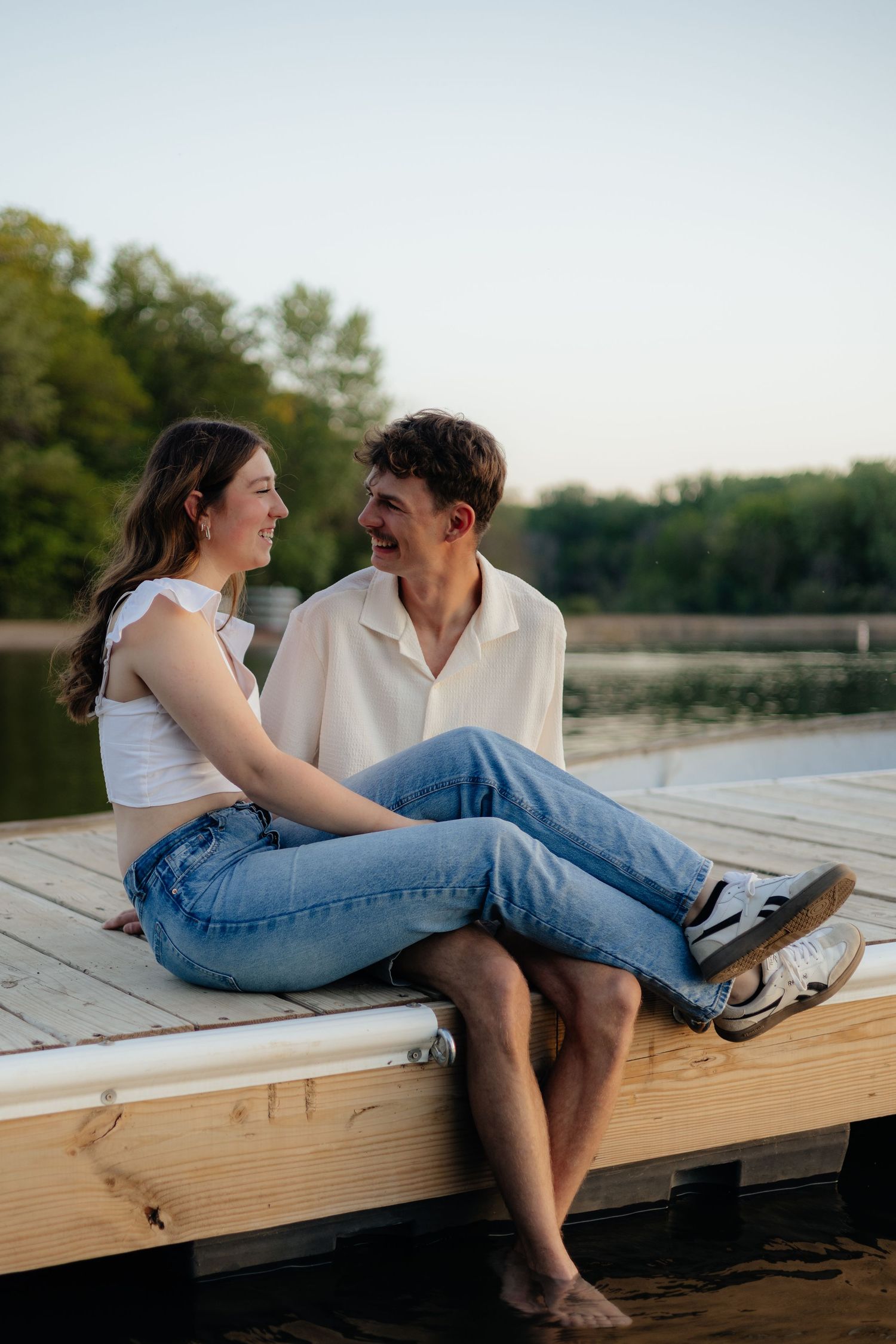 Couple smiling together along the lakeshore at Fish Lake Regional Park in Maple Grove, MN, with bright green trees, clear blue water