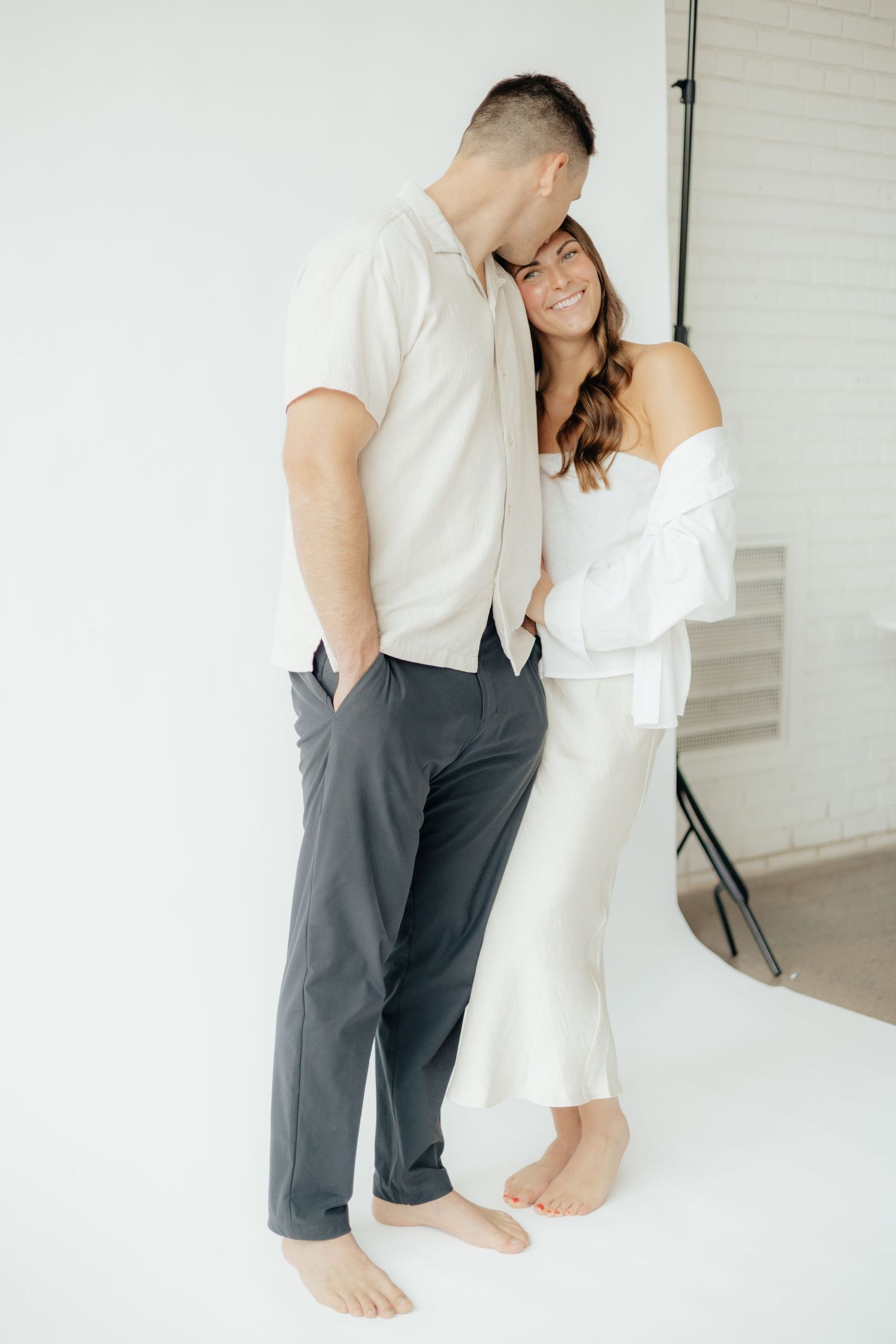 Couple embracing in soft natural light at Abide Studio in Minneapolis, MN, with minimalist white walls and warm, cozy tones