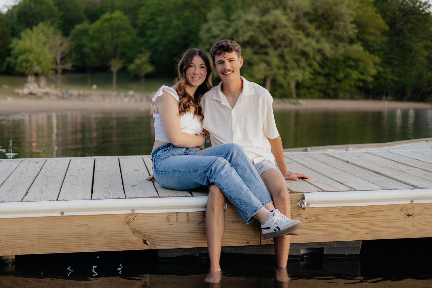 Couple smiling together along the lakeshore at Fish Lake Regional Park in Maple Grove, MN, with bright green trees, clear blue water