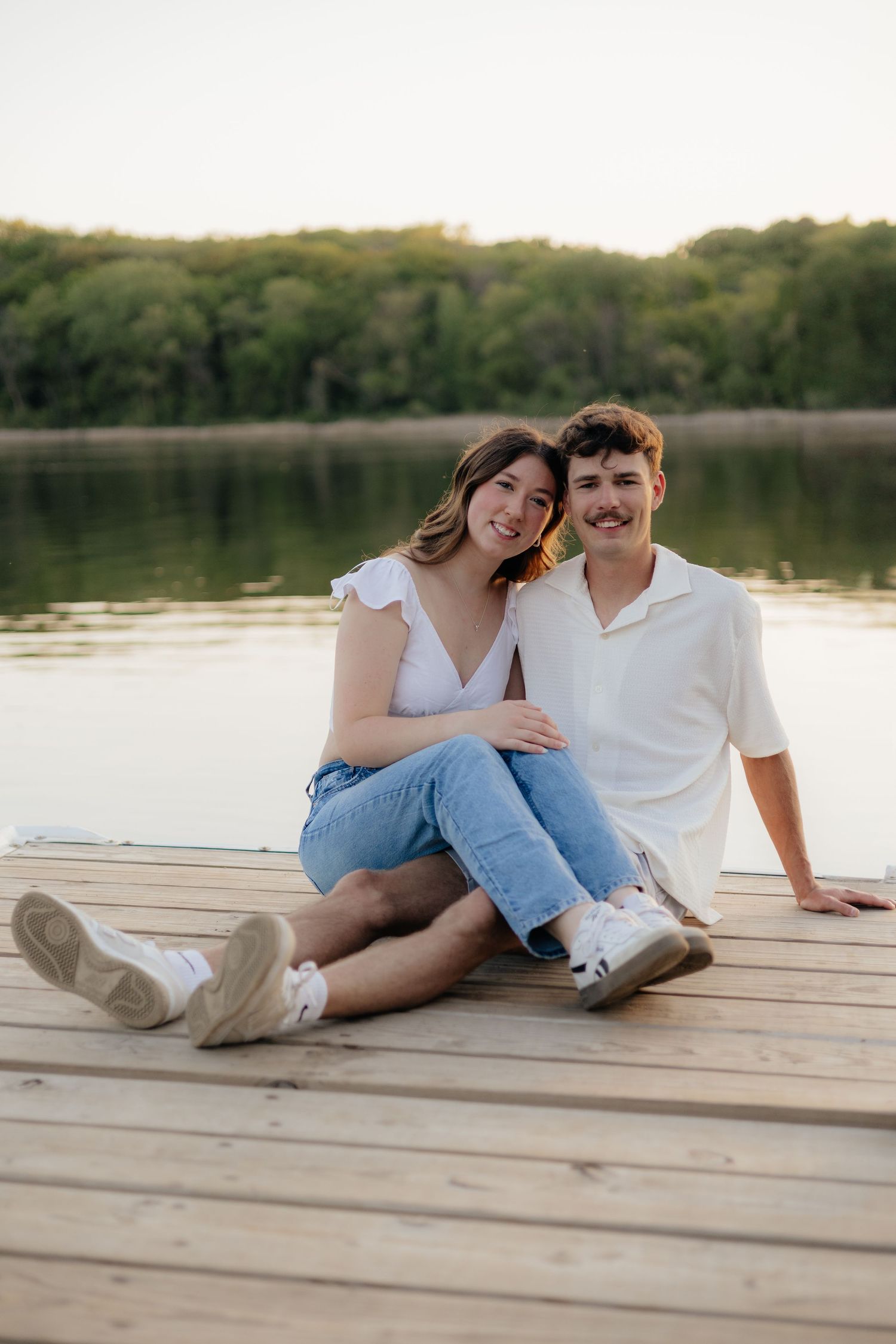 Couple smiling together along the lakeshore at Fish Lake Regional Park in Maple Grove, MN, with bright green trees and clear blue water