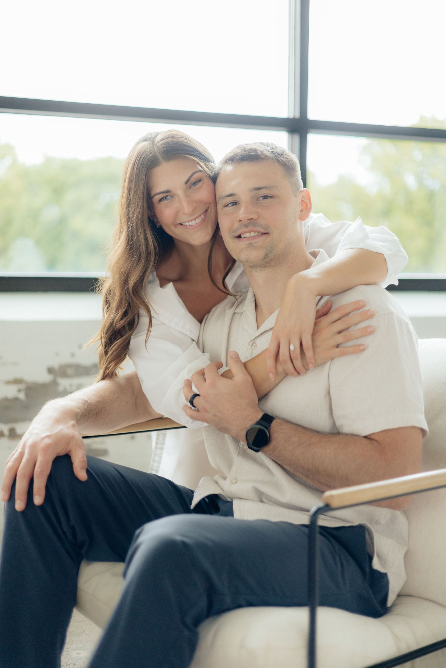 Couple embracing in soft natural light at Abide Studio in Minneapolis, MN, with minimalist white walls and warm, cozy tones