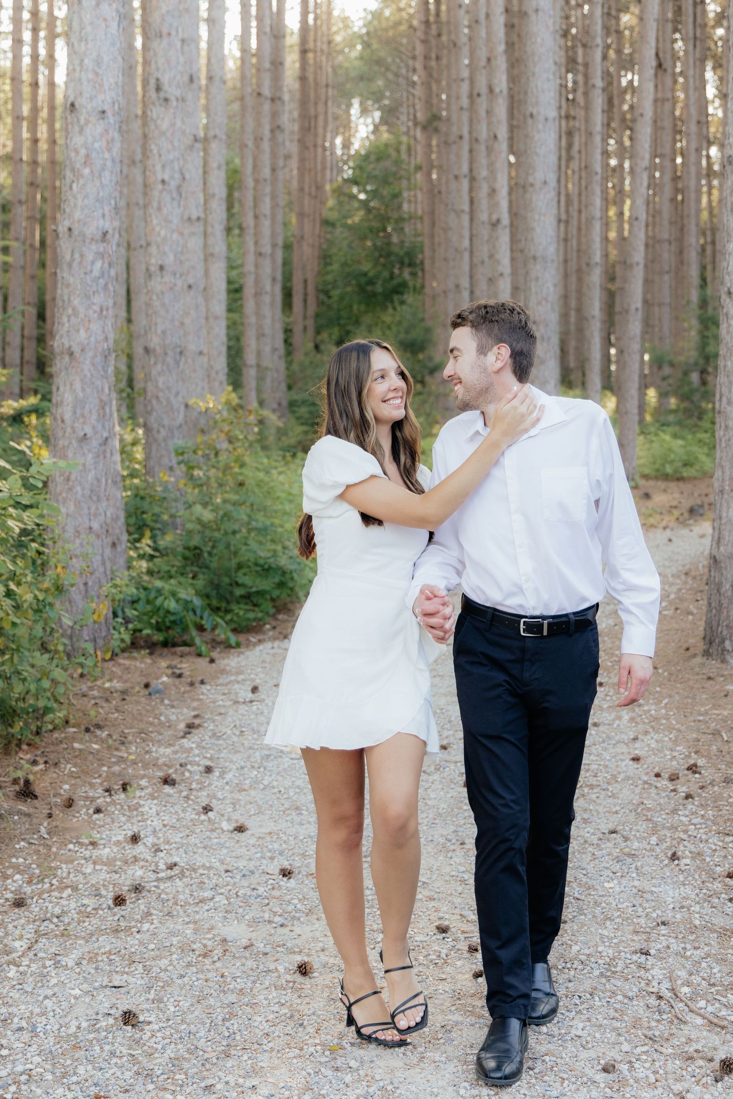 Golden-hour portrait of a couple embracing among tall trees at Pinewood in Cambridge, showcasing woodsy elegance.
