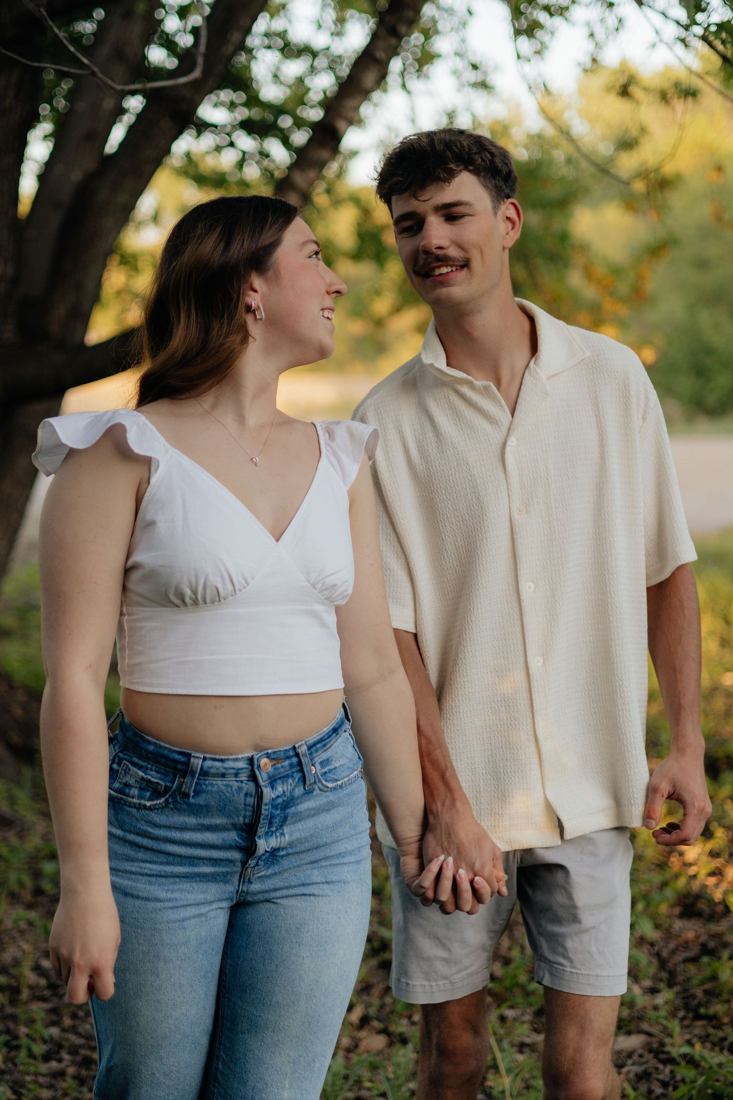 Couple smiling together along the lakeshore at Fish Lake Regional Park in Maple Grove, MN, with bright green trees and clear blue water