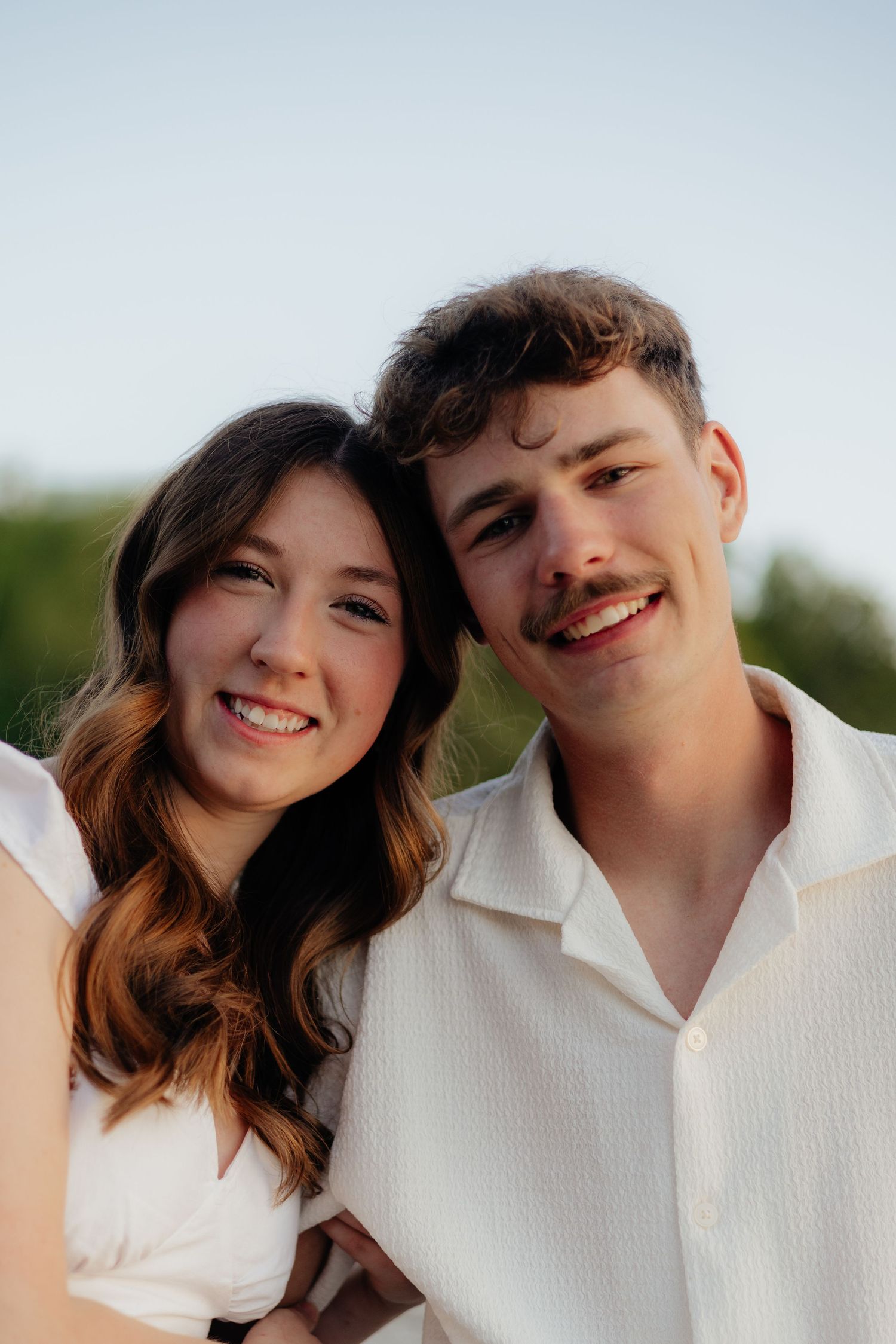 Couple smiling together along the lakeshore at Fish Lake Regional Park in Maple Grove, MN, with bright green trees, clear blue water
