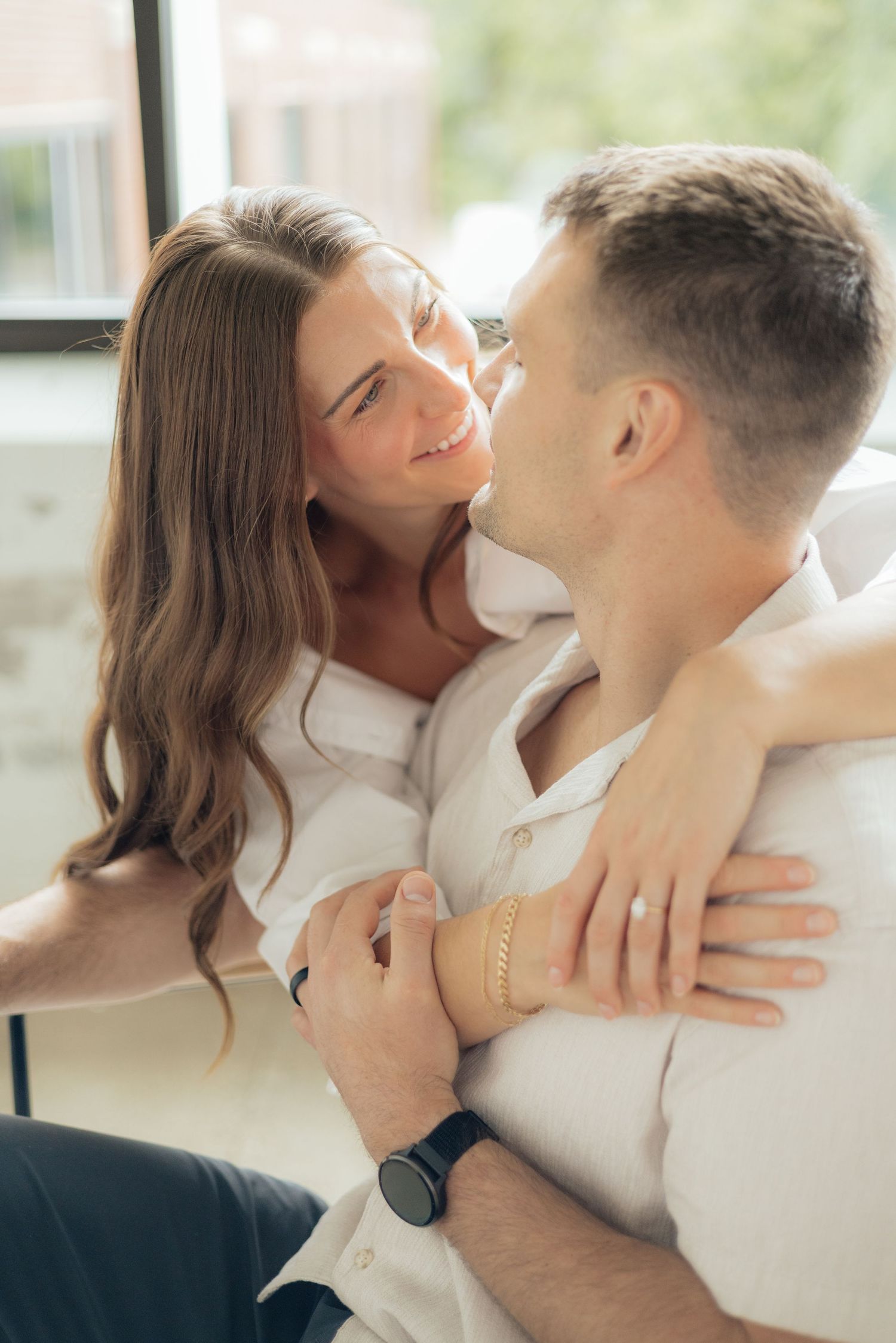 Couple embracing in soft natural light at Abide Studio in Minneapolis, MN, with minimalist white walls and warm, cozy tones