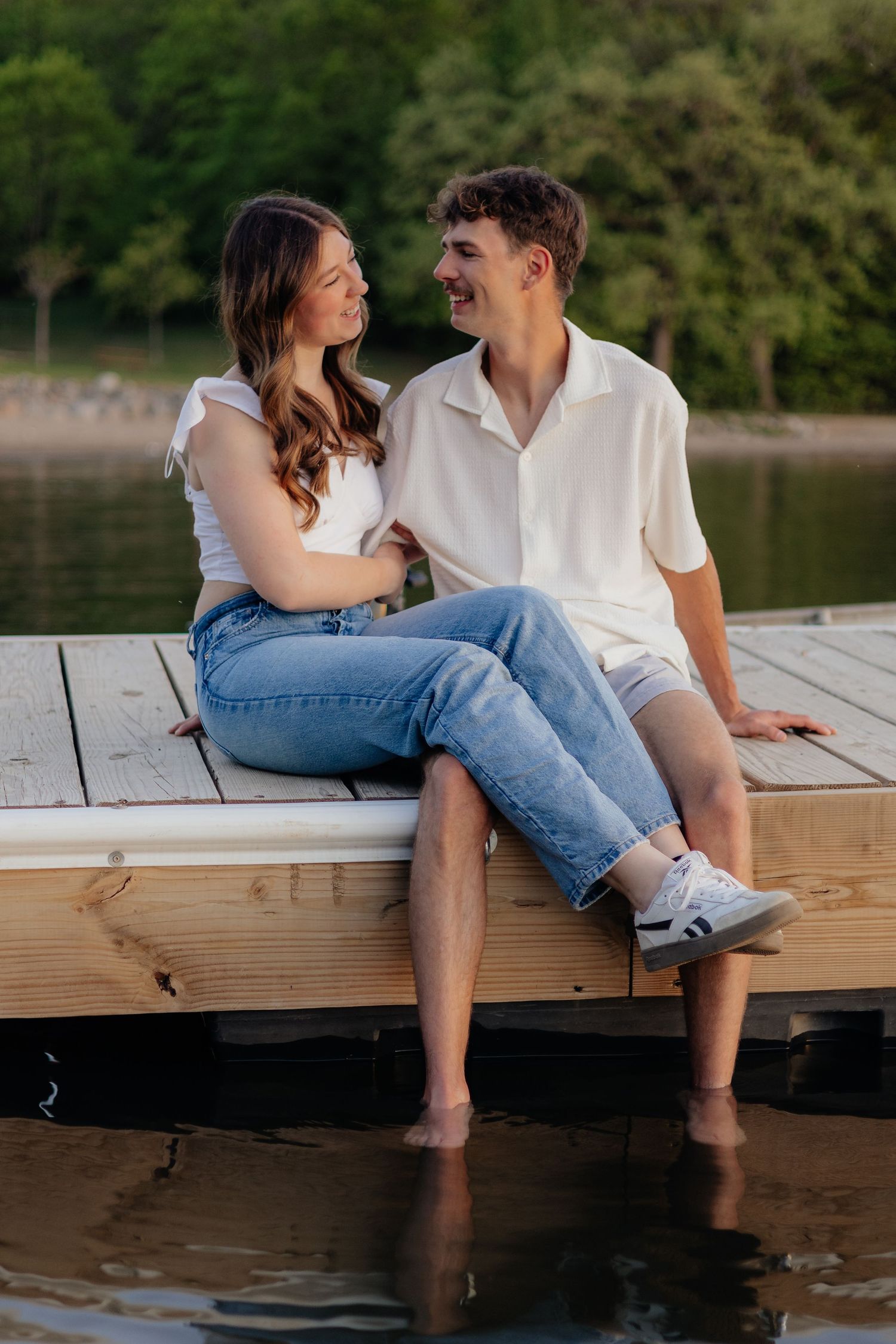 Couple smiling together along the lakeshore at Fish Lake Regional Park in Maple Grove, MN, with bright green trees, clear blue water