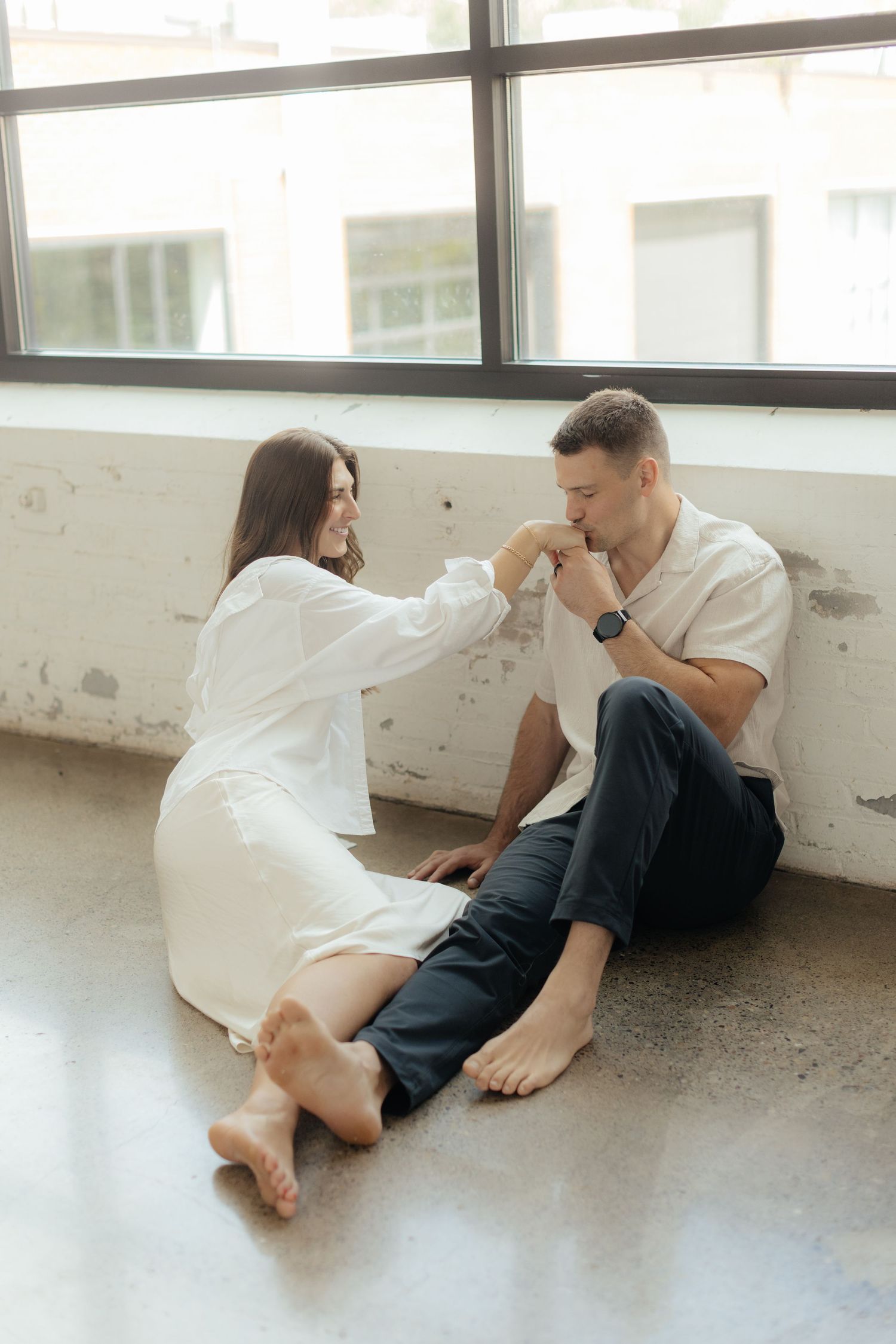 Couple embracing in soft natural light at Abide Studio in Minneapolis, MN, with minimalist white walls and warm, cozy tones