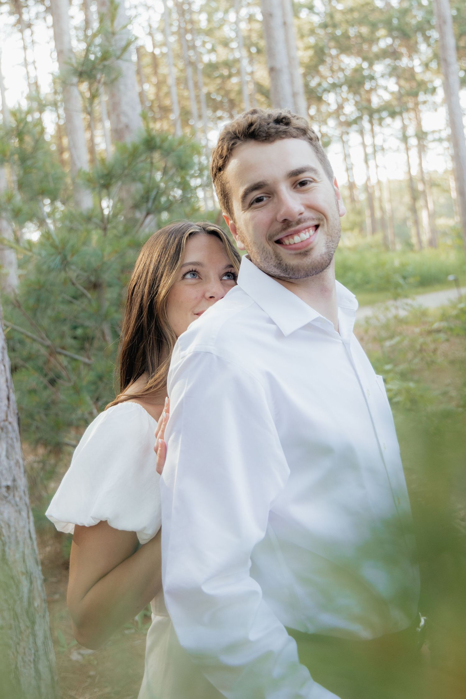 Golden-hour portrait of a couple embracing among tall trees at Pinewood in Cambridge, showcasing woodsy elegance.