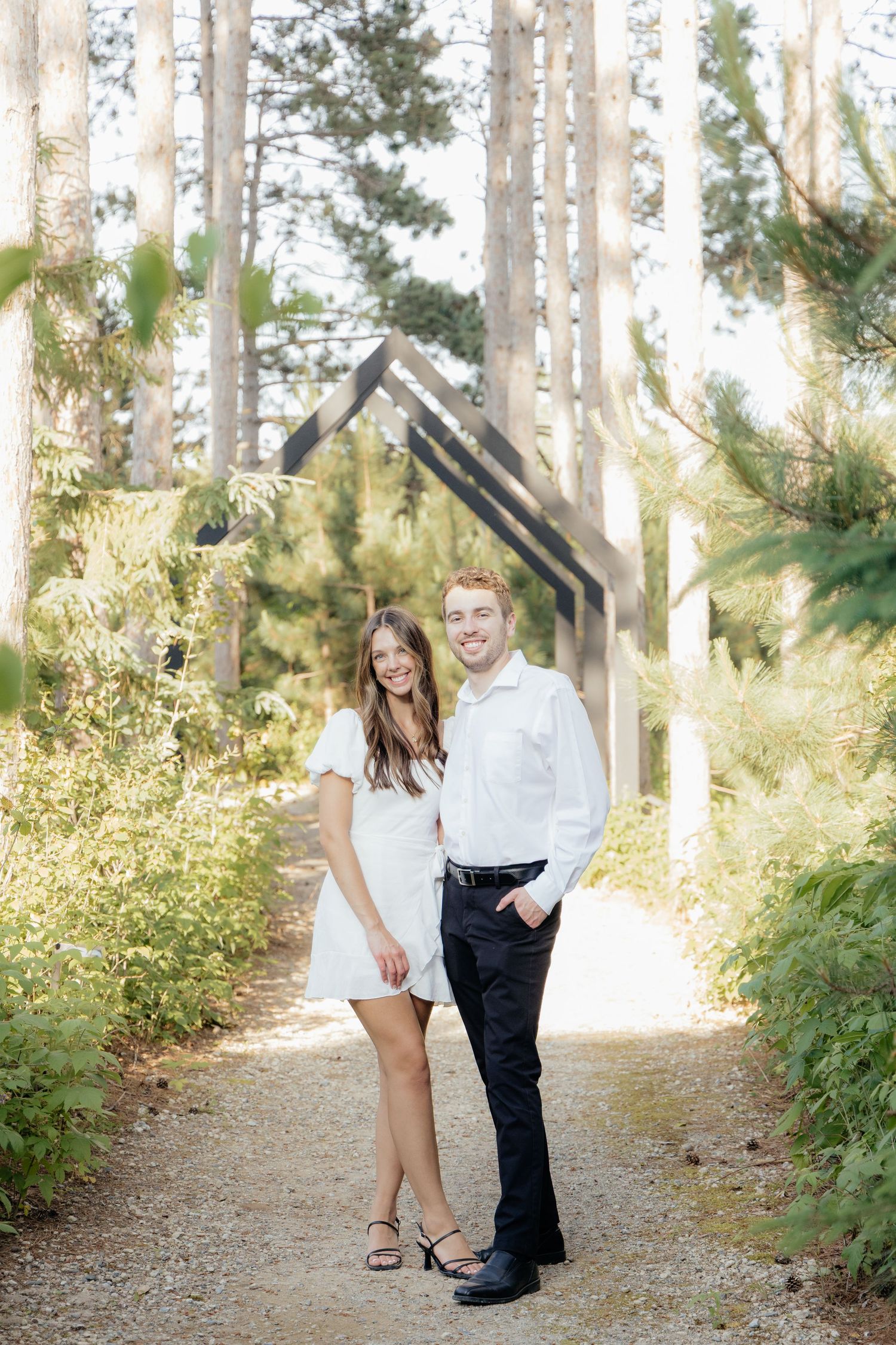 Golden-hour portrait of a couple embracing among tall trees at Pinewood in Cambridge, showcasing woodsy elegance.