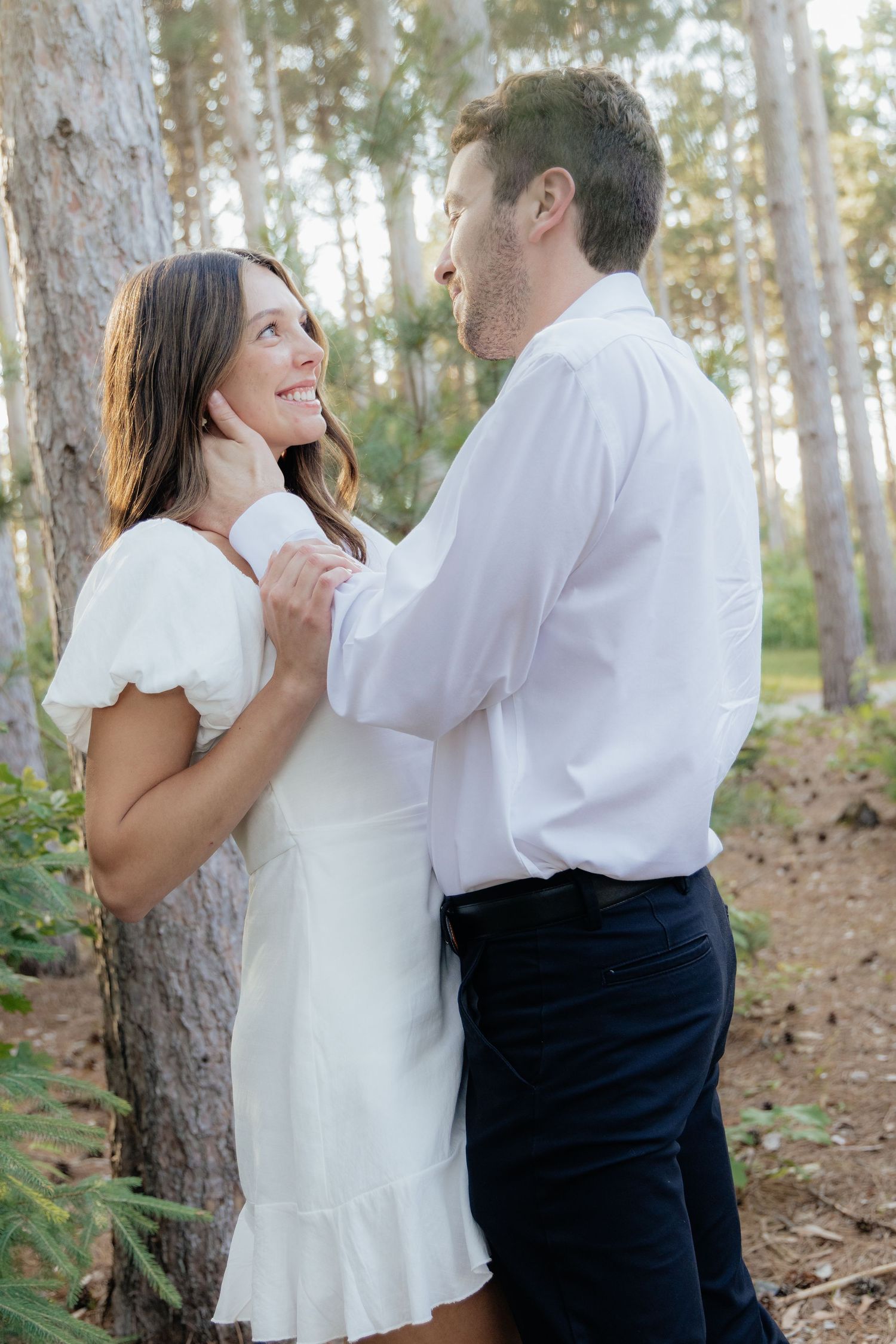 Golden-hour portrait of a couple embracing among tall trees at Pinewood in Cambridge, showcasing woodsy elegance.