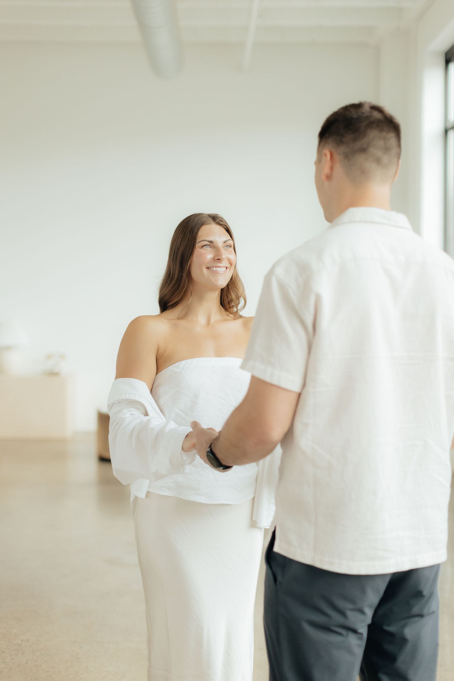 Couple embracing in soft natural light at Abide Studio in Minneapolis, MN, with minimalist white walls and warm, cozy tones
