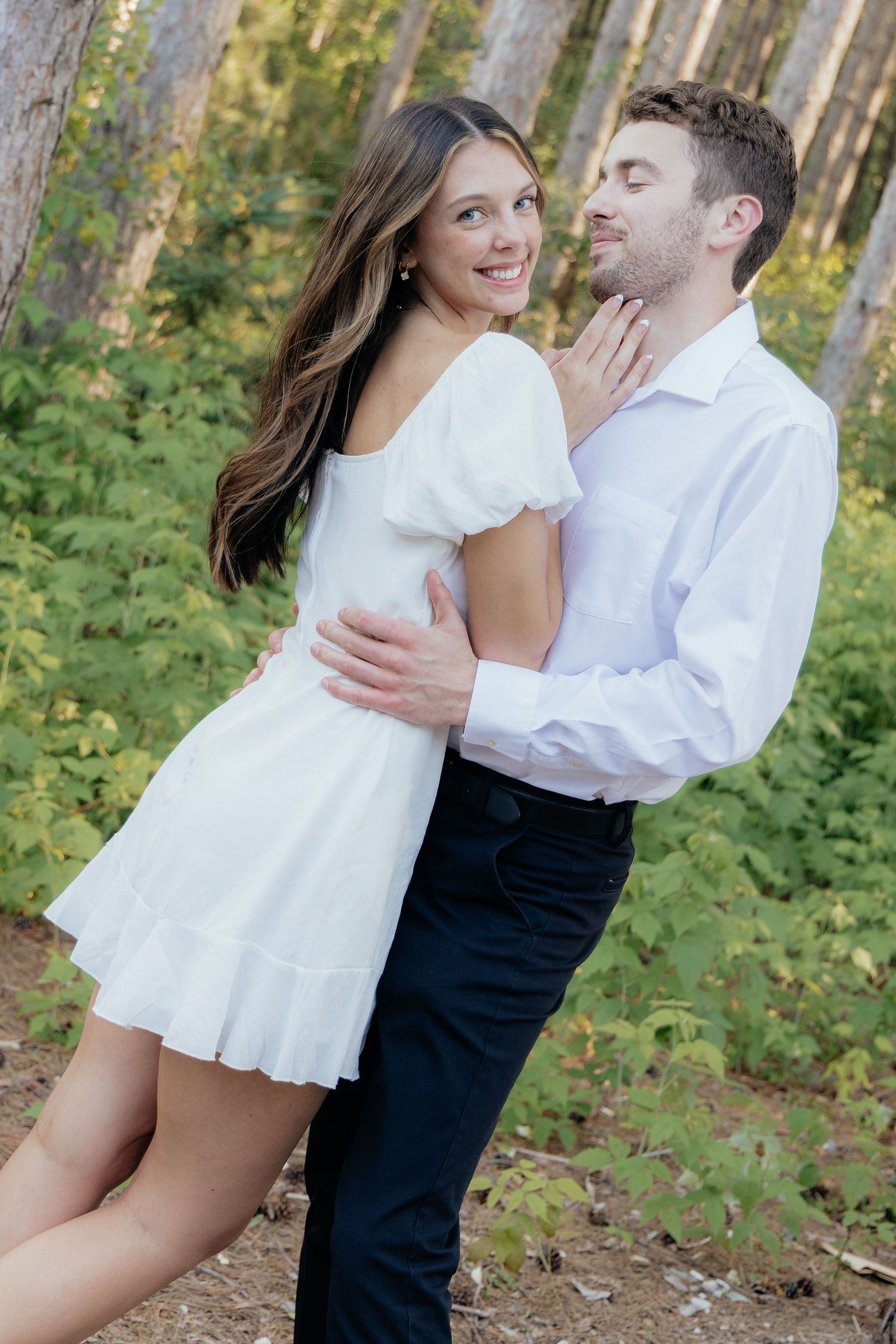 Golden-hour portrait of a couple embracing among tall trees at Pinewood in Cambridge, showcasing woodsy elegance.