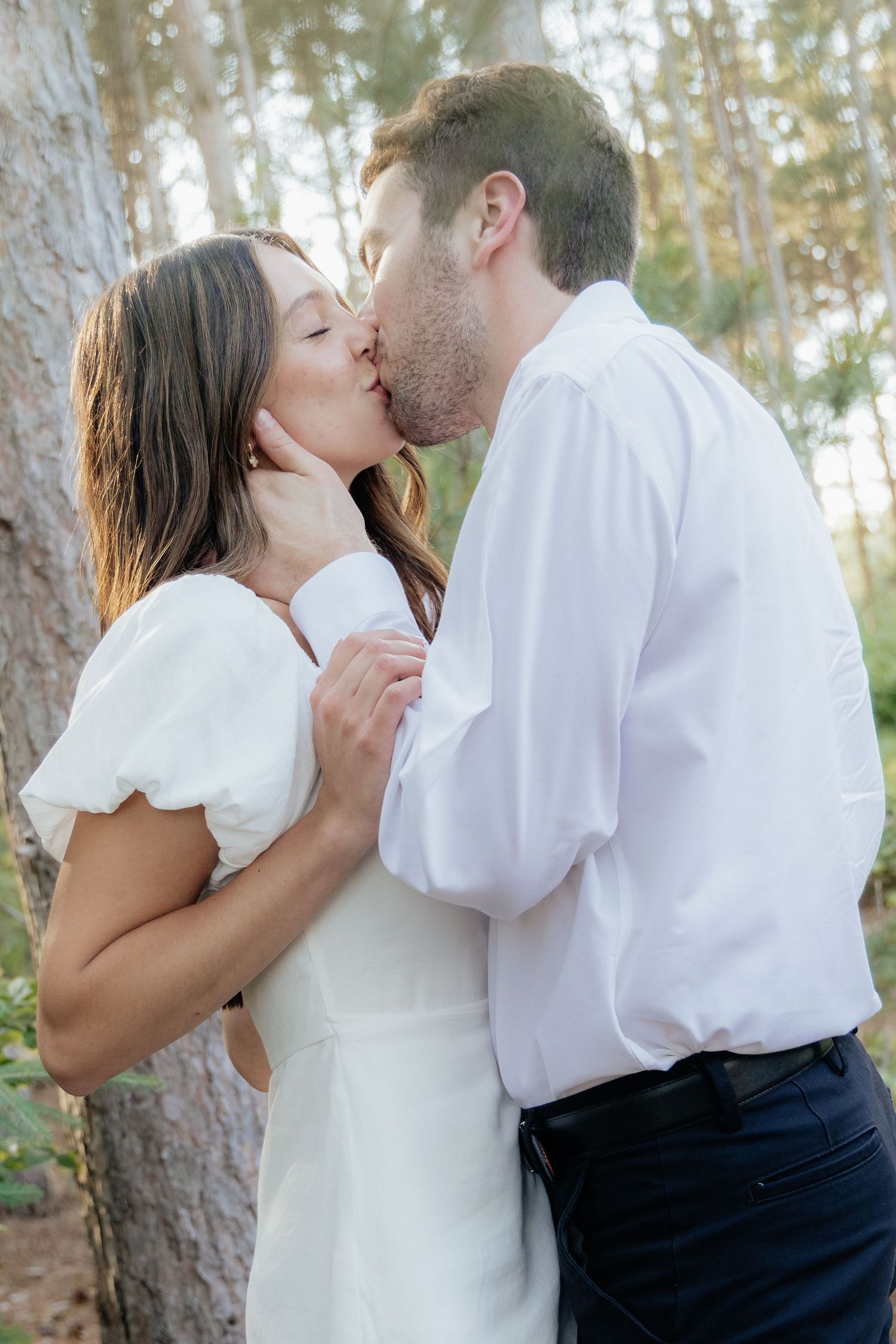 Golden-hour portrait of a couple embracing among tall trees at Pinewood in Cambridge, showcasing woodsy elegance.