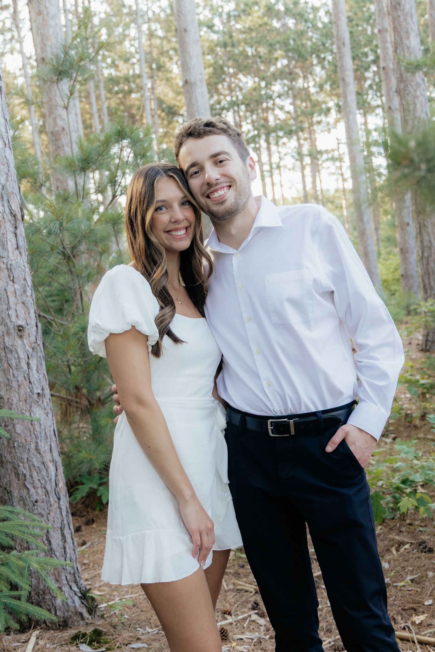 Golden-hour portrait of a couple embracing among tall trees at Pinewood in Cambridge, showcasing woodsy elegance.