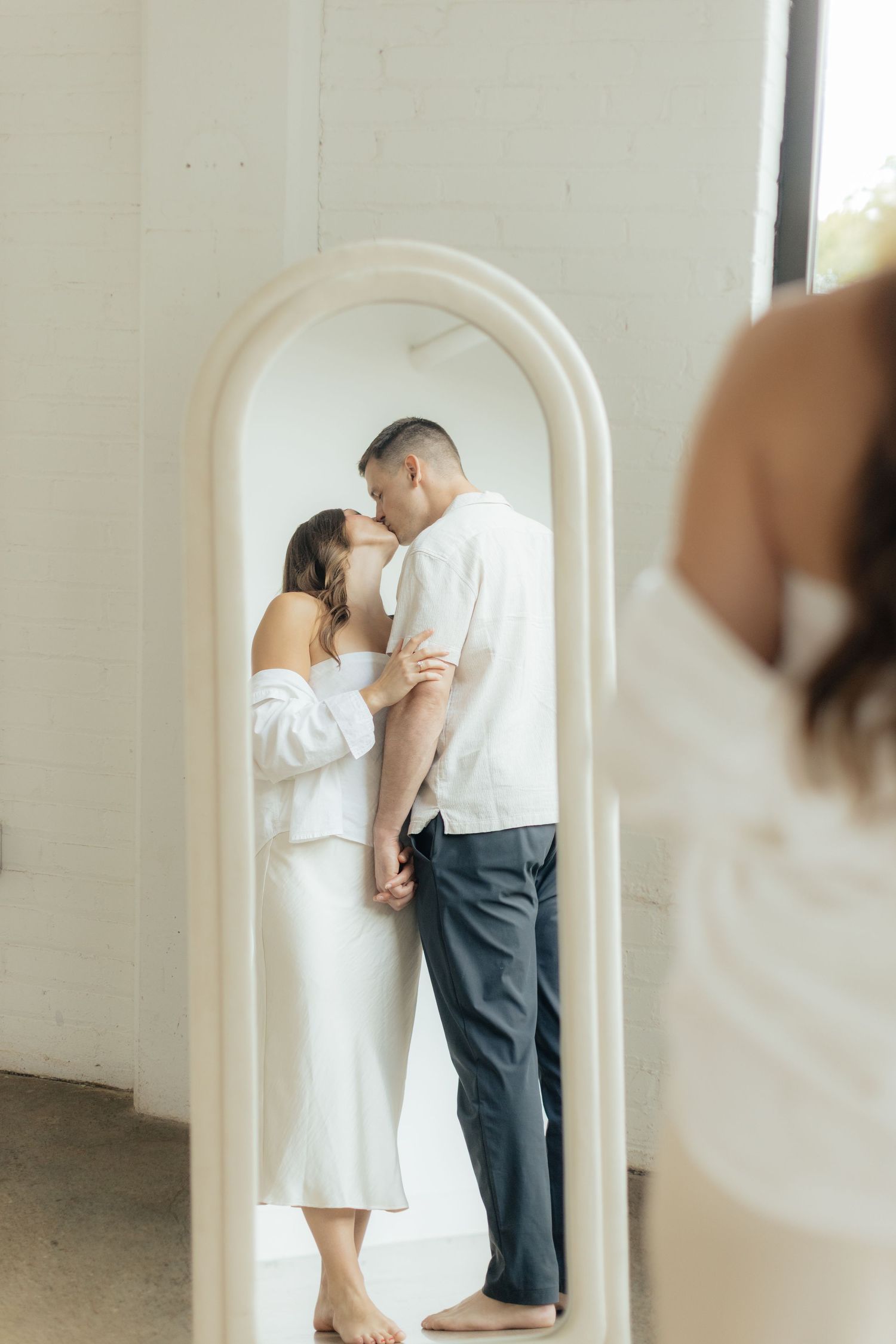 Couple embracing in soft natural light at Abide Studio in Minneapolis, MN, with minimalist white walls and warm, cozy tones