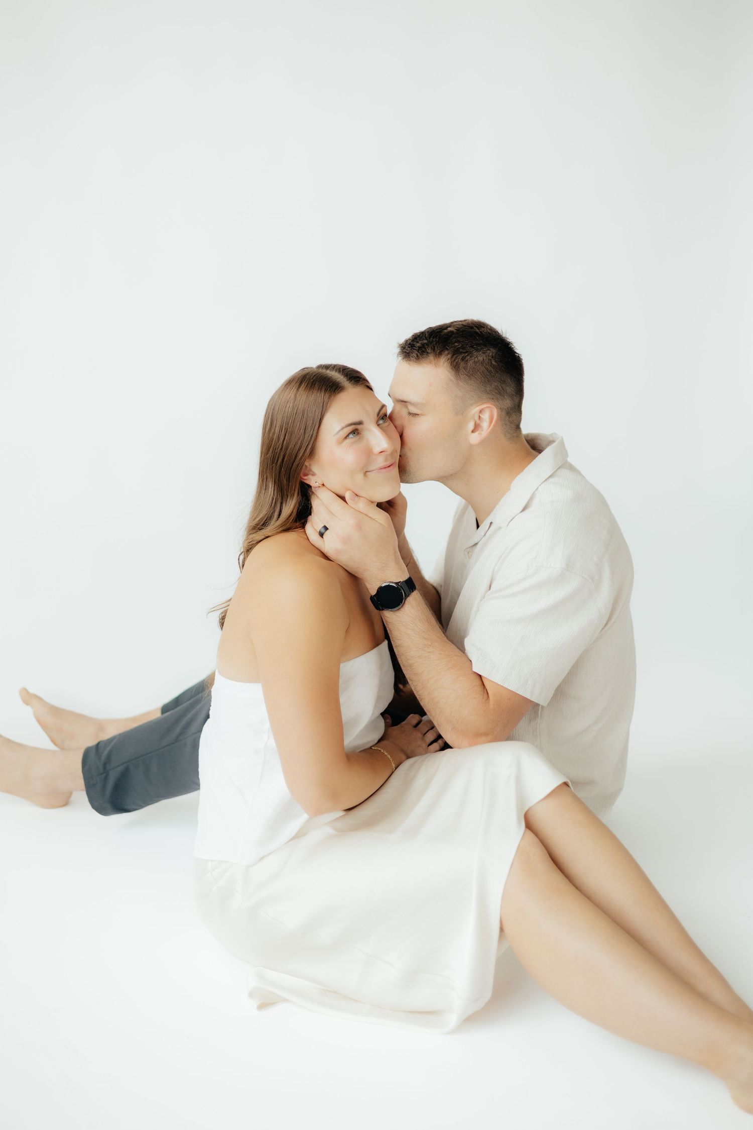 Couple embracing in soft natural light at Abide Studio in Minneapolis, MN, with minimalist white walls and warm, cozy tones