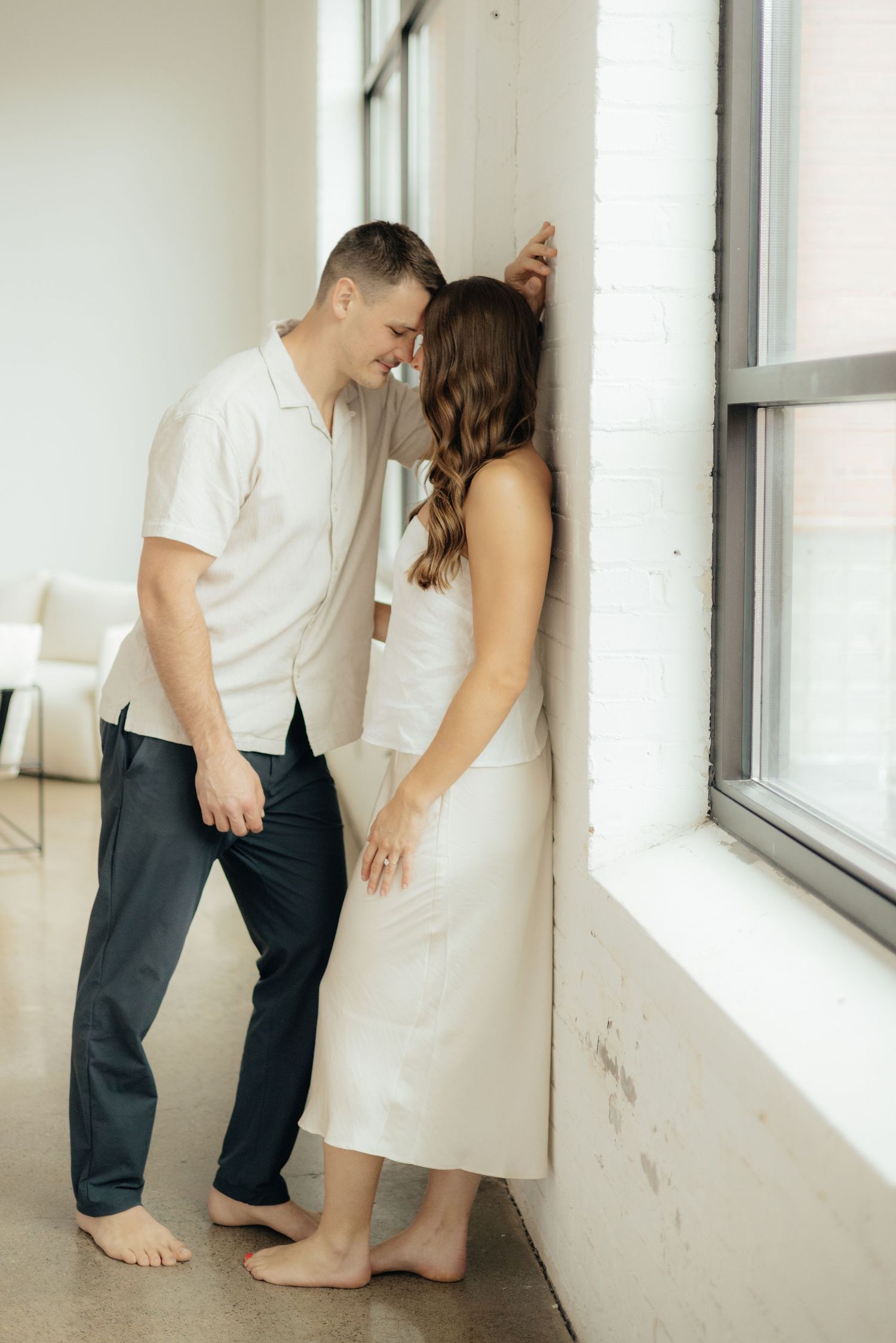 Couple embracing in soft natural light at Abide Studio in Minneapolis, MN, with minimalist white walls and warm, cozy tones