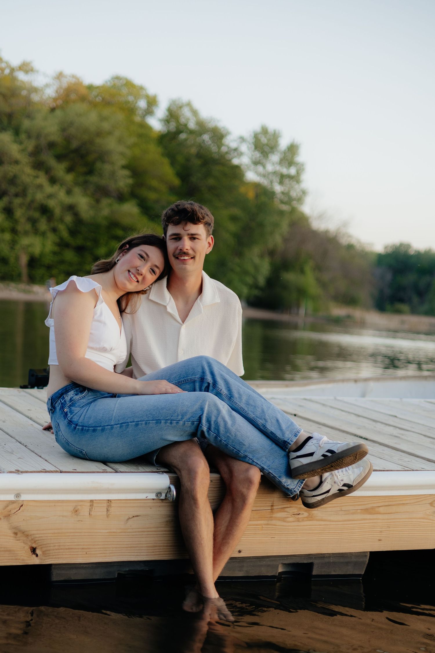 Couple smiling together along the lakeshore at Fish Lake Regional Park in Maple Grove, MN, with bright green trees and clear blue water