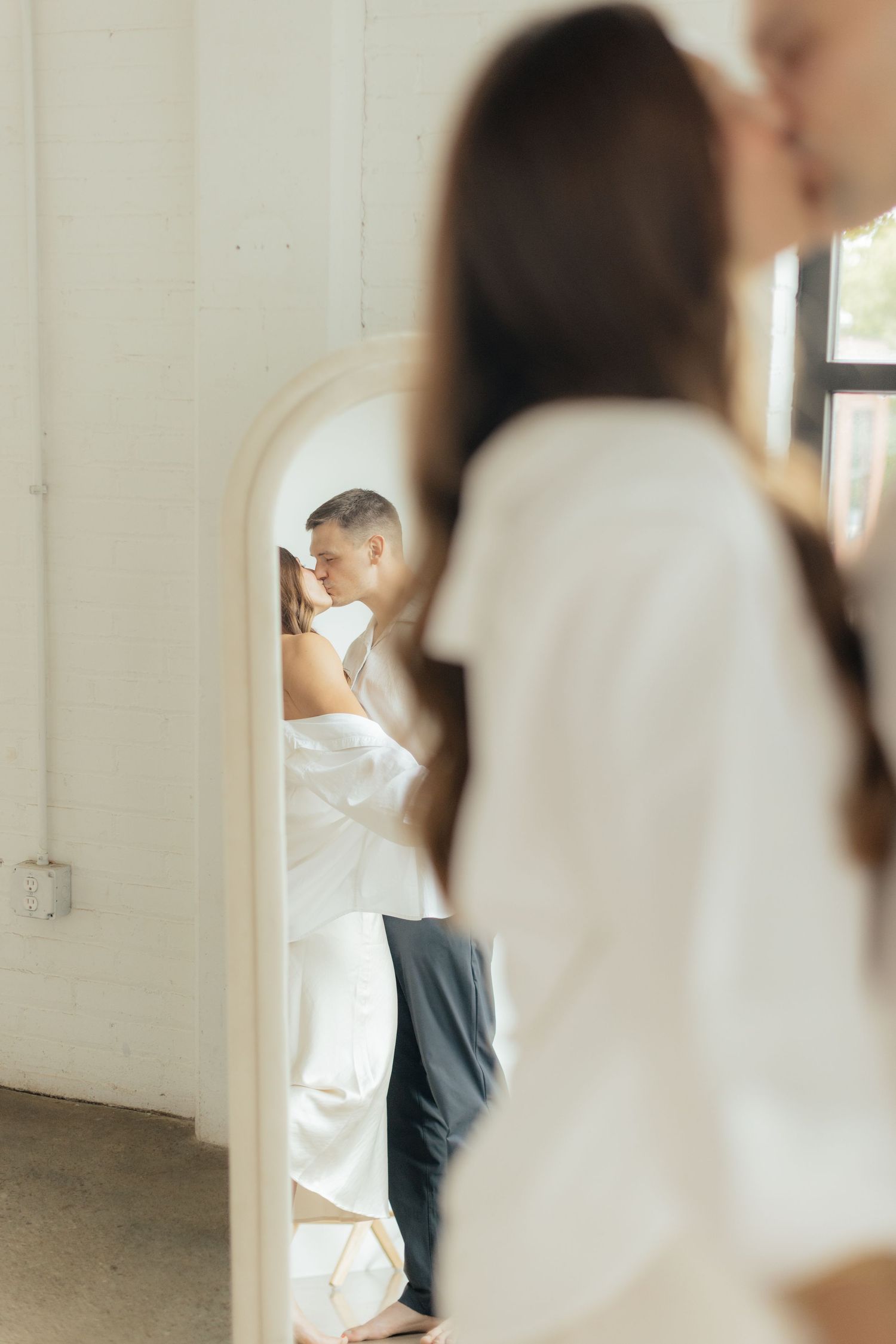 Couple embracing in soft natural light at Abide Studio in Minneapolis, MN, with minimalist white walls and warm, cozy tones
