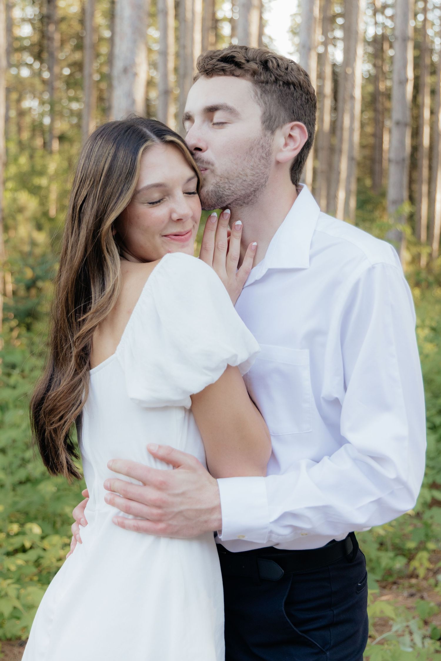Golden-hour portrait of a couple embracing among tall trees at Pinewood in Cambridge, showcasing woodsy elegance.