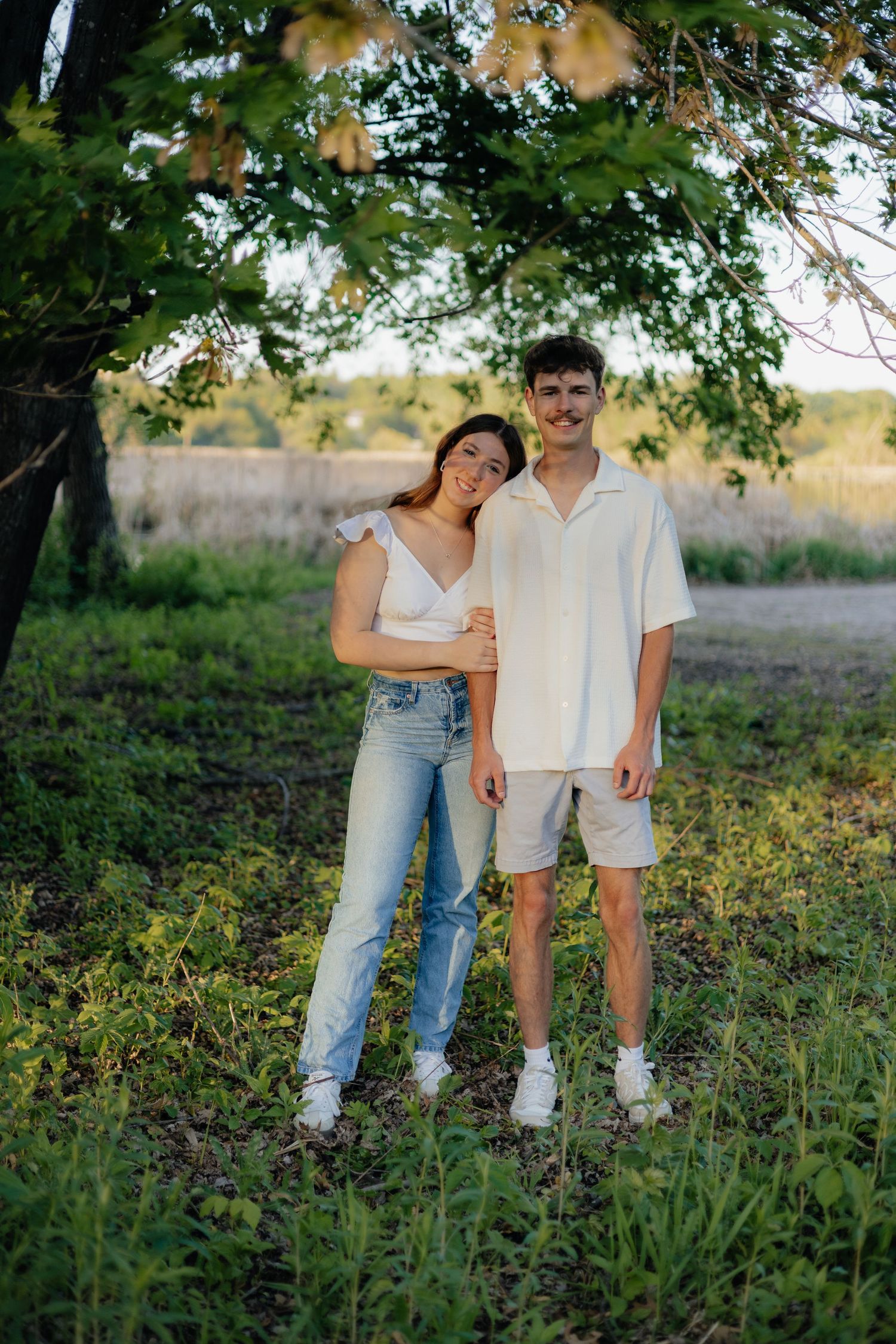 Couple smiling together along the lakeshore at Fish Lake Regional Park in Maple Grove, MN, with bright green trees and clear blue water
