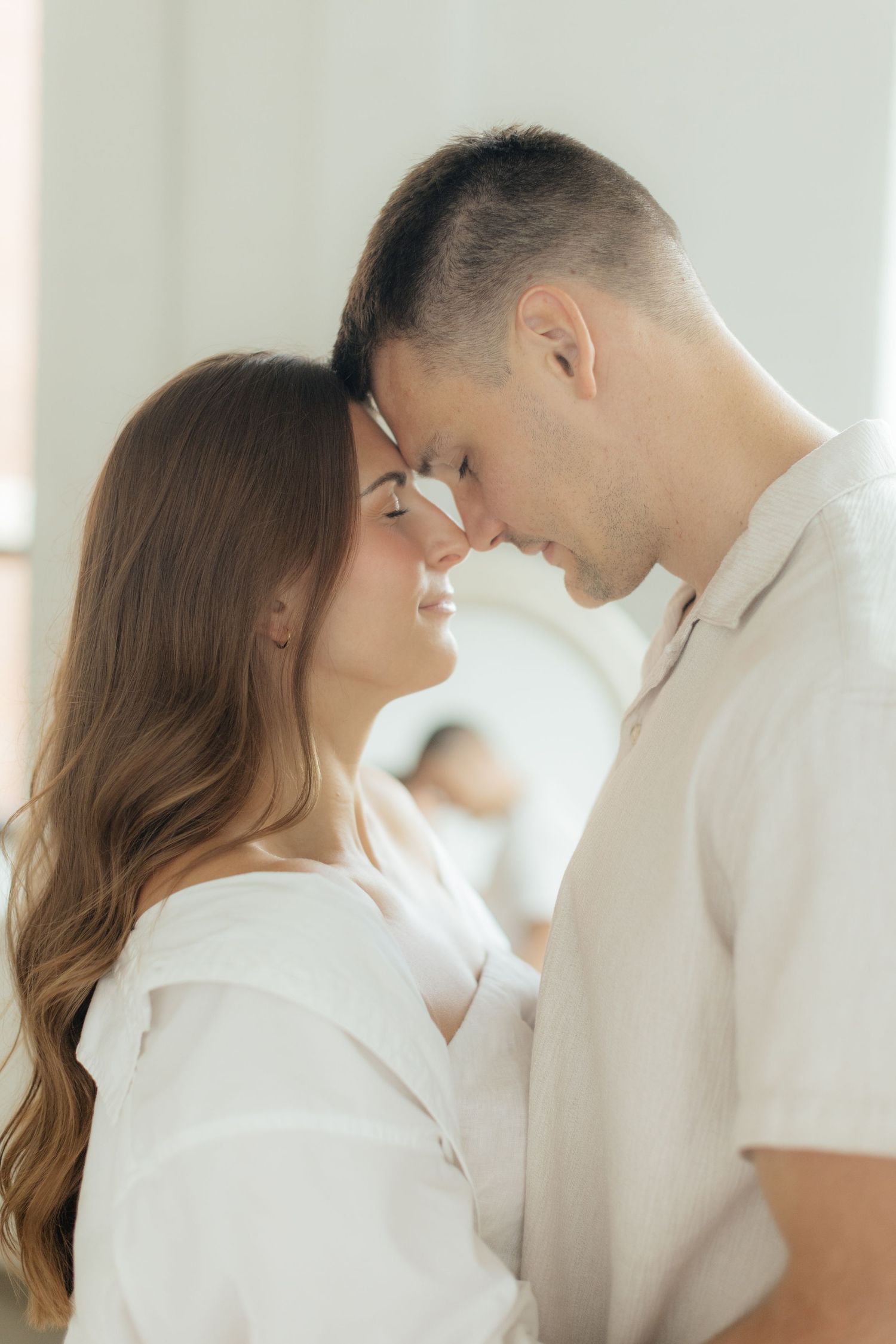 Couple embracing in soft natural light at Abide Studio in Minneapolis, MN, with minimalist white walls and warm, cozy tones
