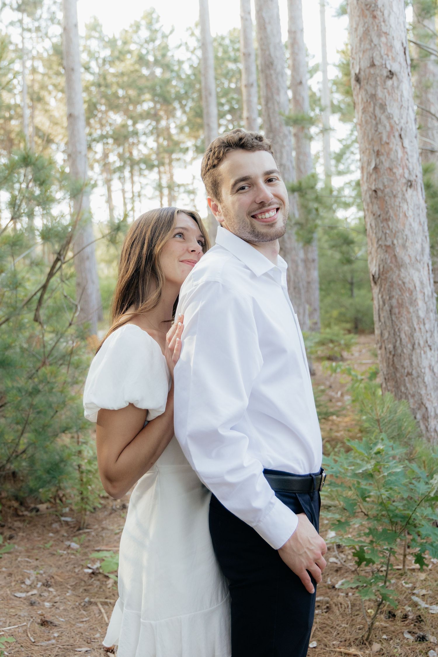 Golden-hour portrait of a couple embracing among tall trees at Pinewood in Cambridge, showcasing woodsy elegance.