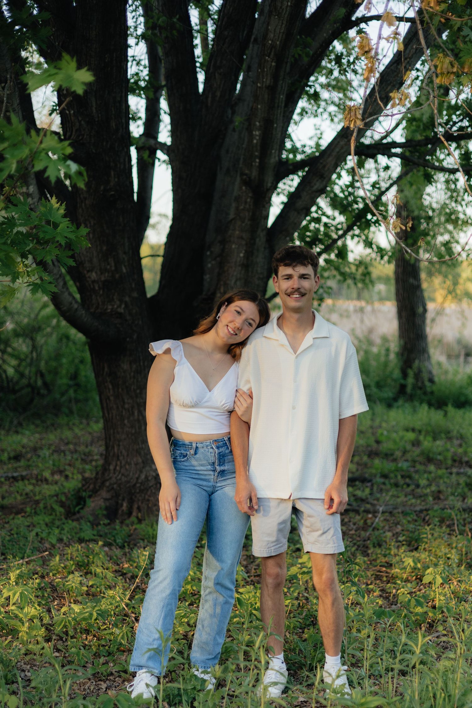 Couple smiling together along the lakeshore at Fish Lake Regional Park in Maple Grove, MN, with bright green trees and clear blue water