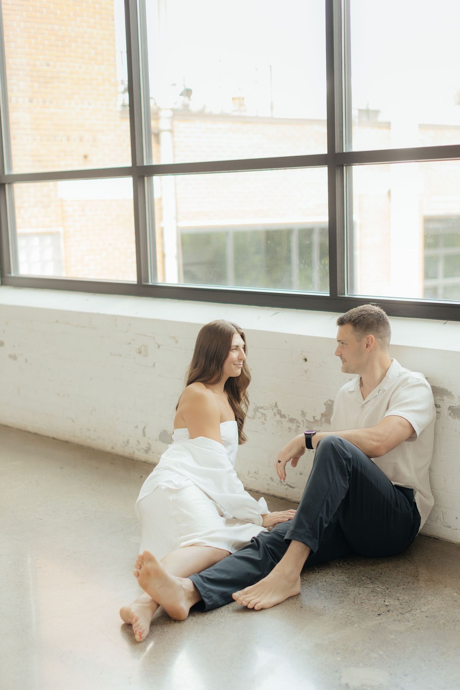 Couple embracing in soft natural light at Abide Studio in Minneapolis, MN, with minimalist white walls and warm, cozy tones