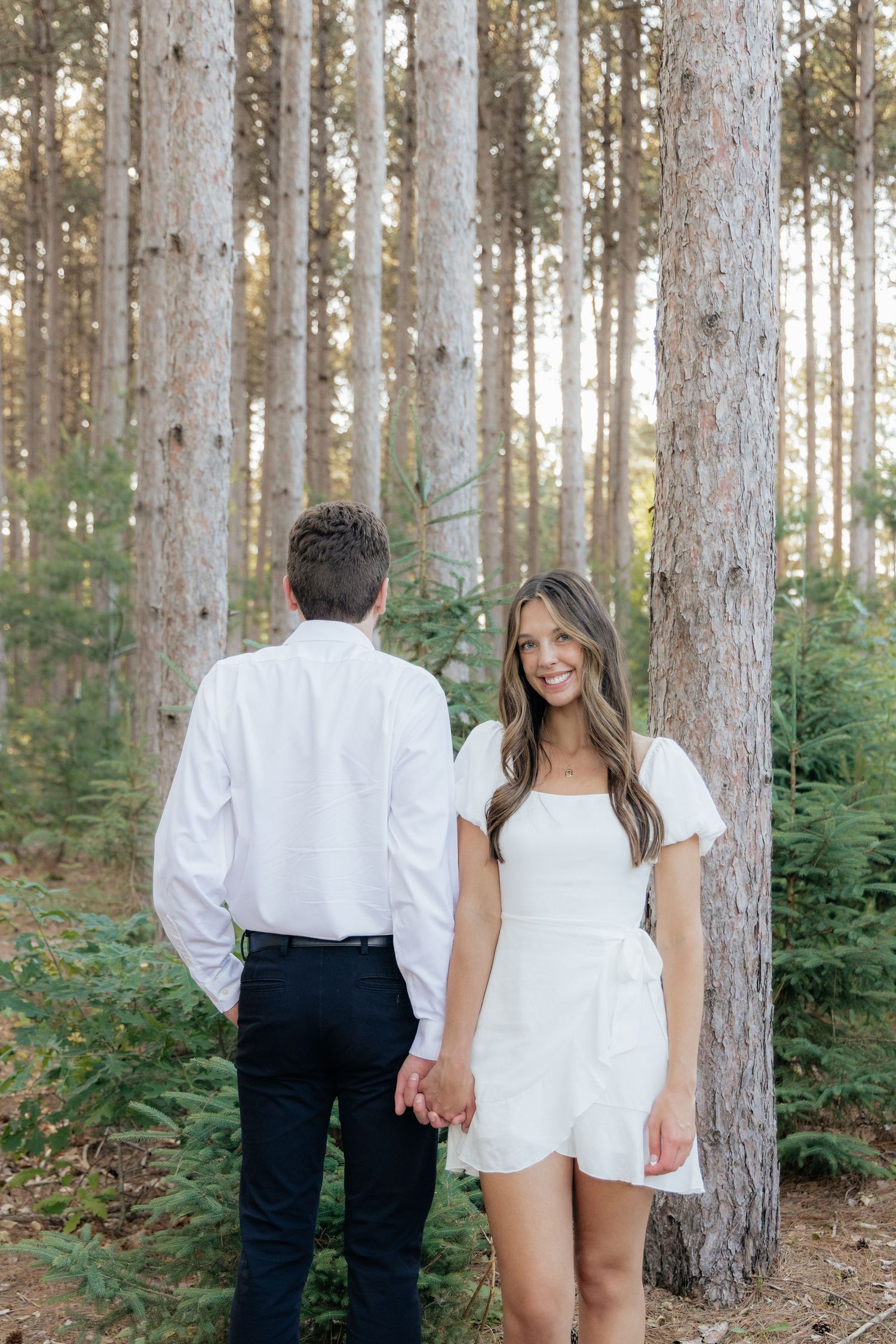Golden-hour portrait of a couple embracing among tall trees at Pinewood in Cambridge, showcasing woodsy elegance.