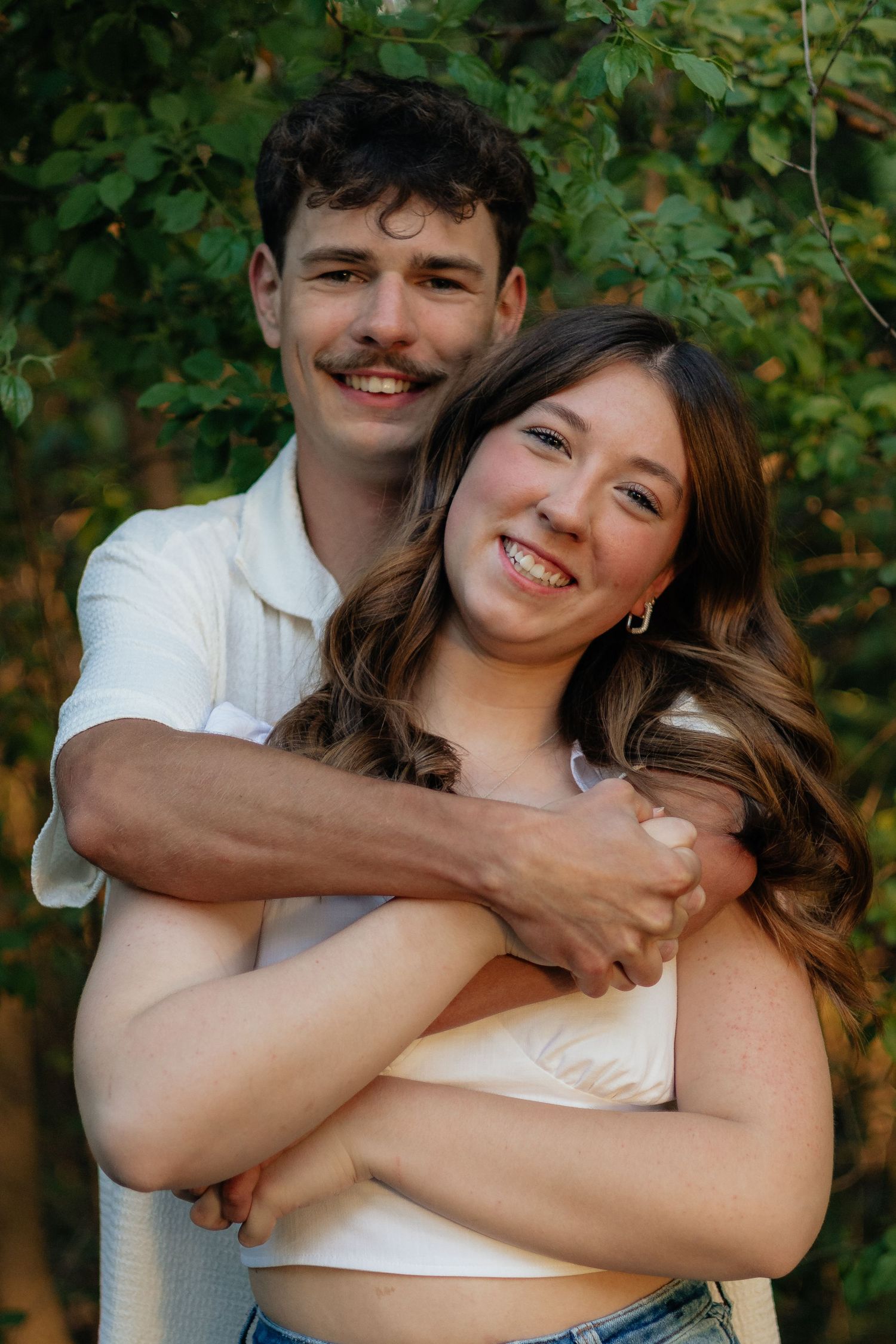 Couple smiling together along the lakeshore at Fish Lake Regional Park in Maple Grove, MN, with bright green trees and clear blue water