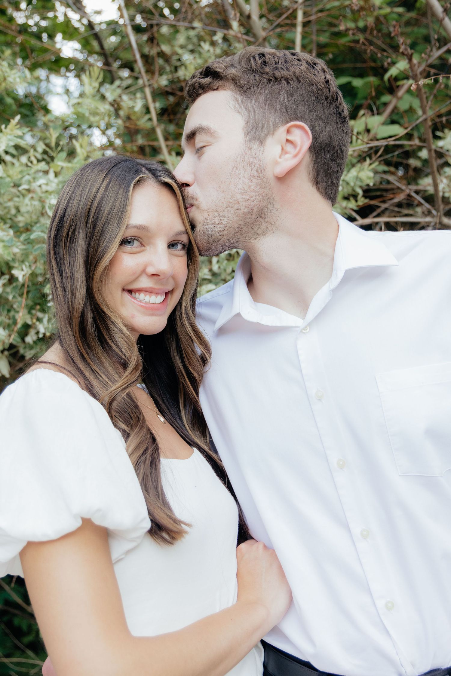 Golden-hour portrait of a couple embracing among tall trees at Pinewood in Cambridge, showcasing woodsy elegance.