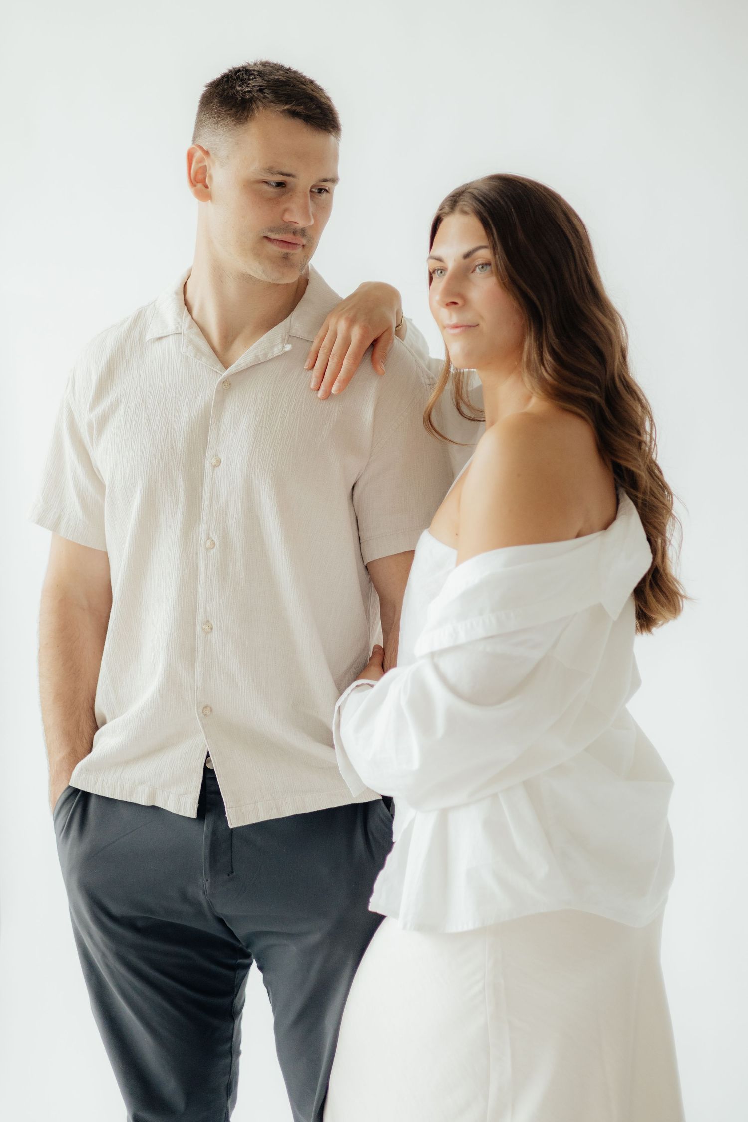 Couple embracing in soft natural light at Abide Studio in Minneapolis, MN, with minimalist white walls and warm, cozy tones