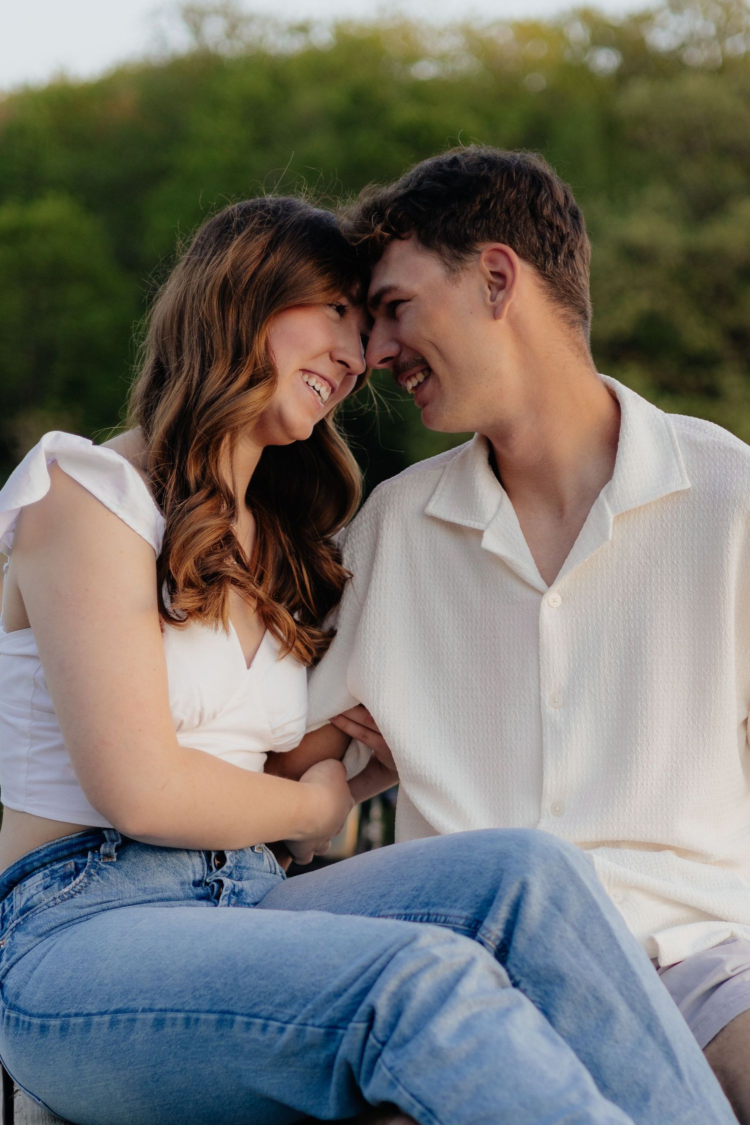 Couple smiling together along the lakeshore at Fish Lake Regional Park in Maple Grove, MN, with bright green trees, clear blue water