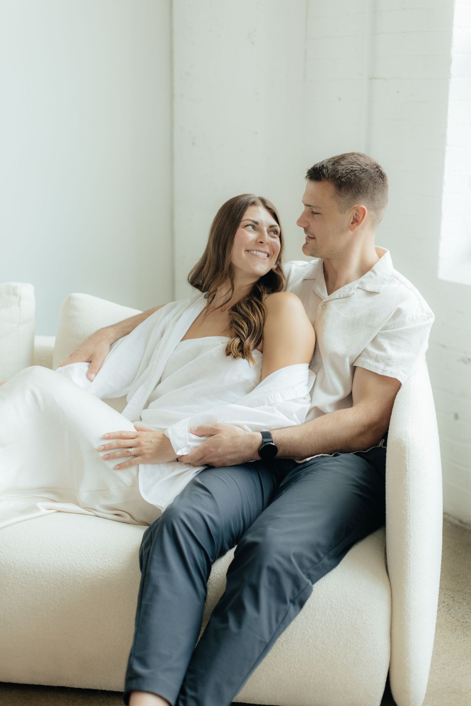 Couple embracing in soft natural light at Abide Studio in Minneapolis, MN, with minimalist white walls and warm, cozy tones