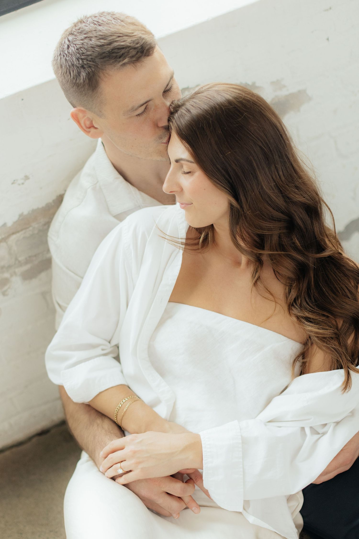 Couple embracing in soft natural light at Abide Studio in Minneapolis, MN, with minimalist white walls and warm, cozy tones