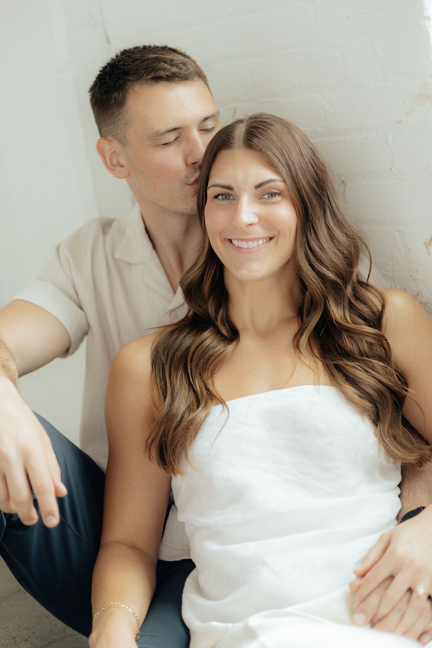 Couple embracing in soft natural light at Abide Studio in Minneapolis, MN, with minimalist white walls and warm, cozy tones