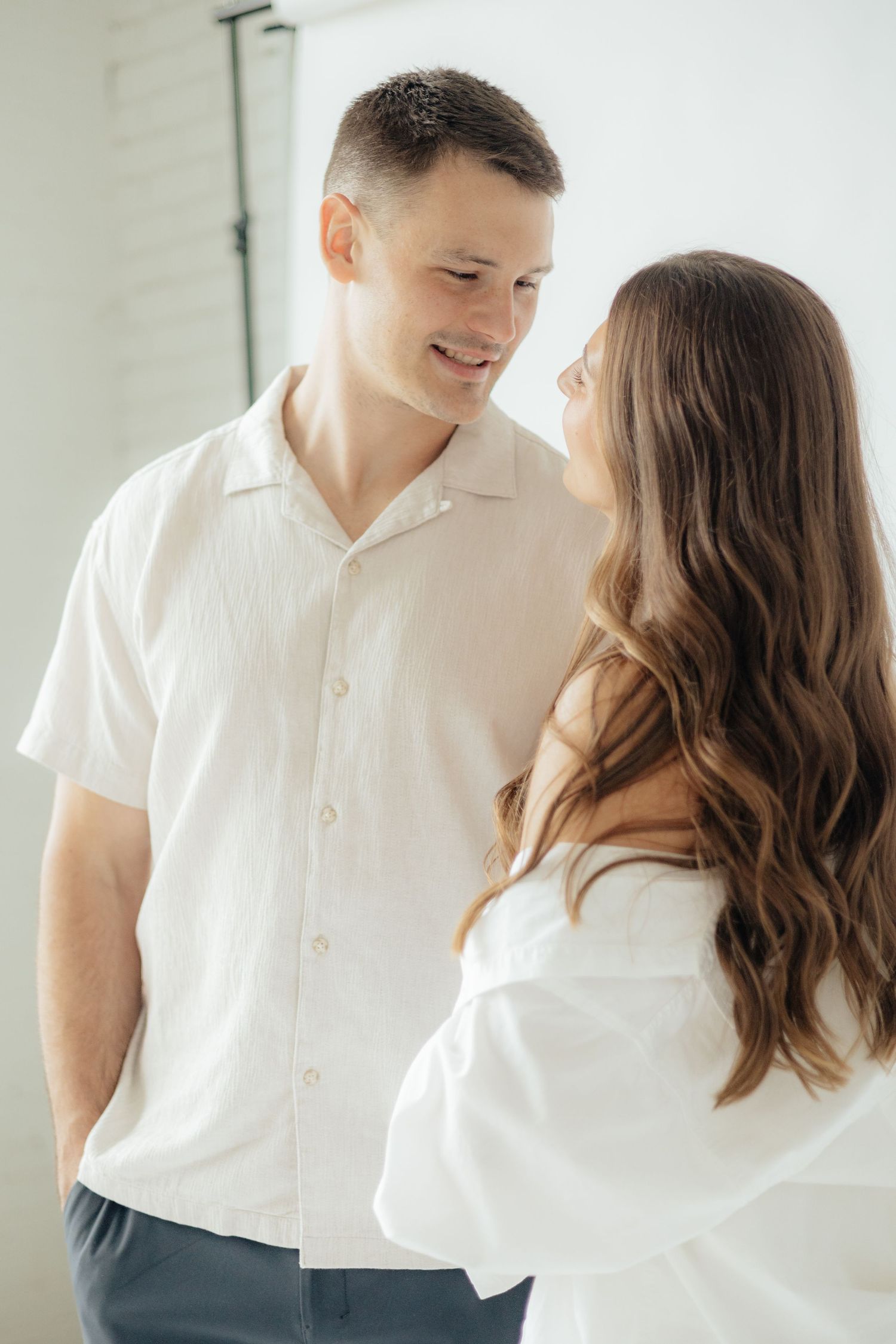 Couple embracing in soft natural light at Abide Studio in Minneapolis, MN, with minimalist white walls and warm, cozy tones