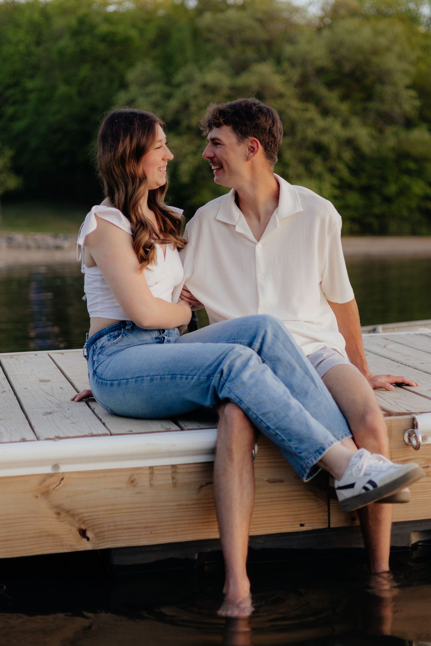 Couple smiling together along the lakeshore at Fish Lake Regional Park in Maple Grove, MN, with bright green trees, clear blue water