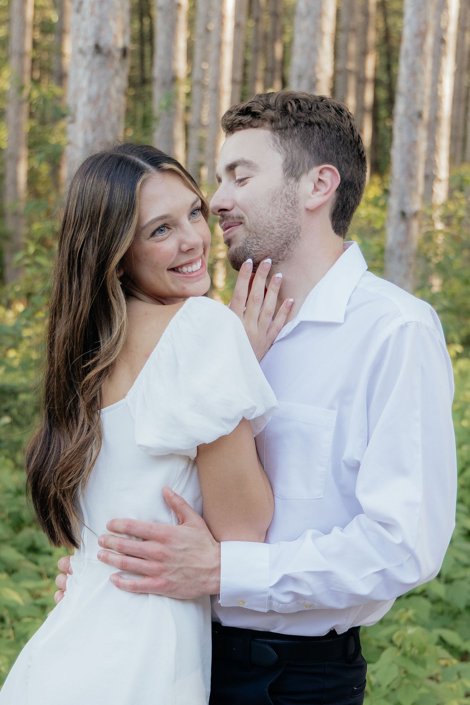 Golden-hour portrait of a couple embracing among tall trees at Pinewood in Cambridge, showcasing woodsy elegance.