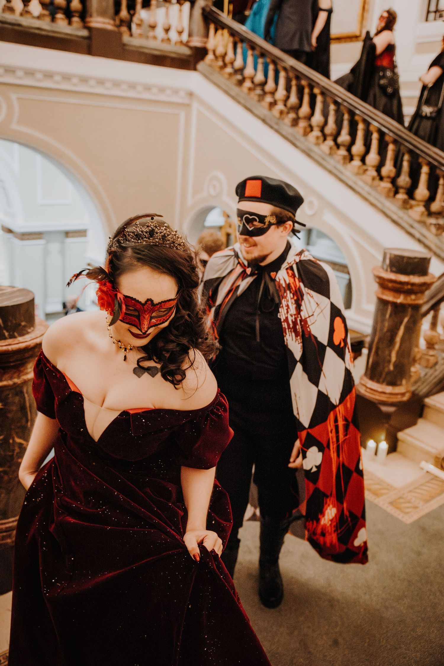 Couple in vintage-inspired masquerade costumes descending an ornate staircase at a fantasy ball.