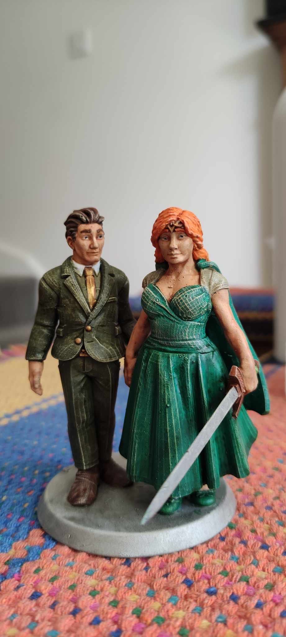 Painted figurines of a couple in formal attire, with the woman wearing a teal dress holding a sword.