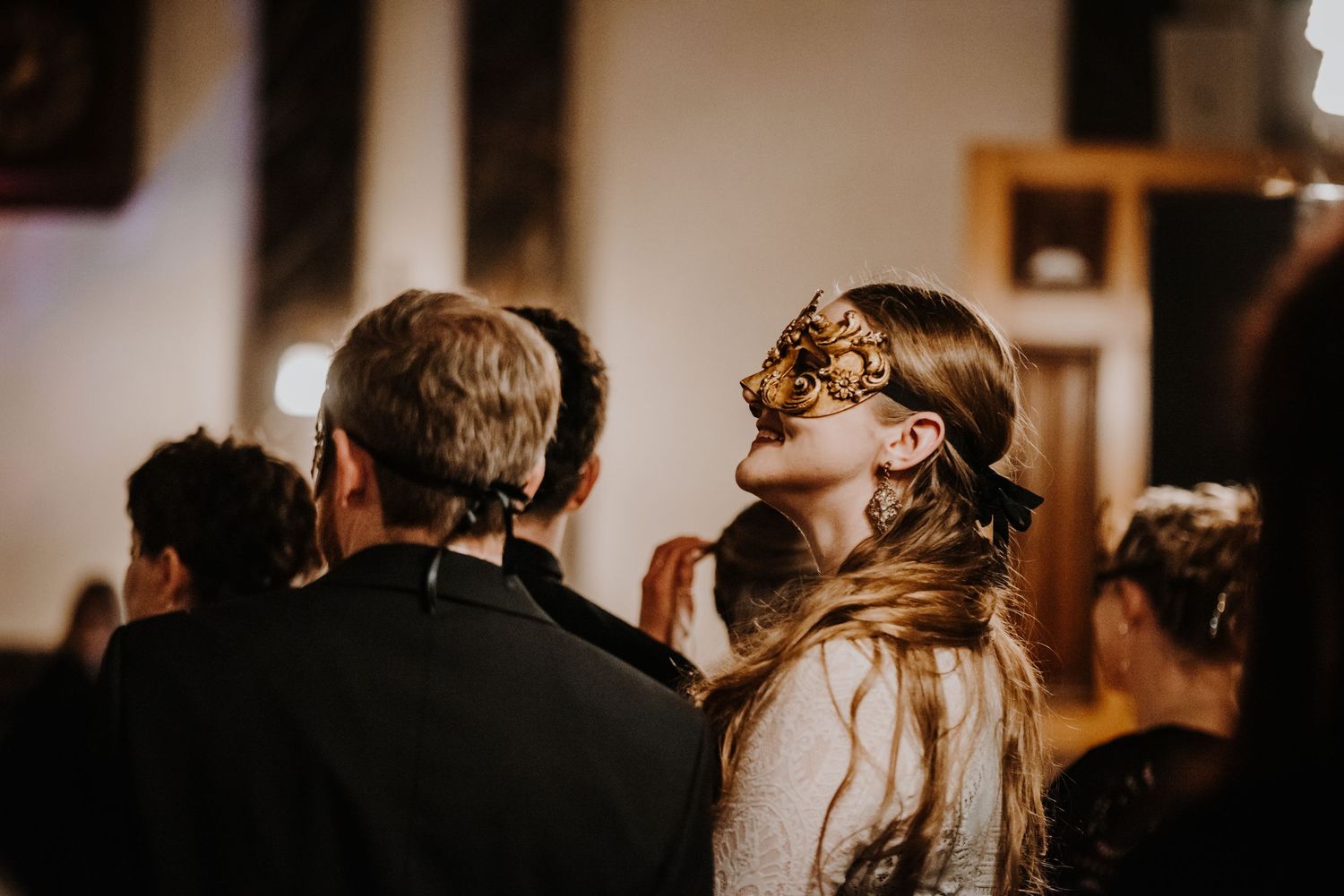 Guests in formal attire wearing ornate masks at a fantasy ball.