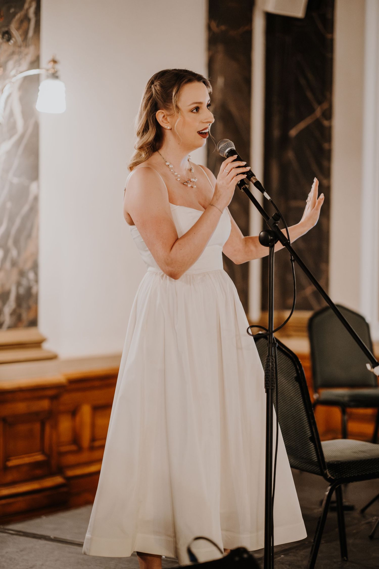 Young performer in white dress sings on stage during an indoor event at a fantasy ball.