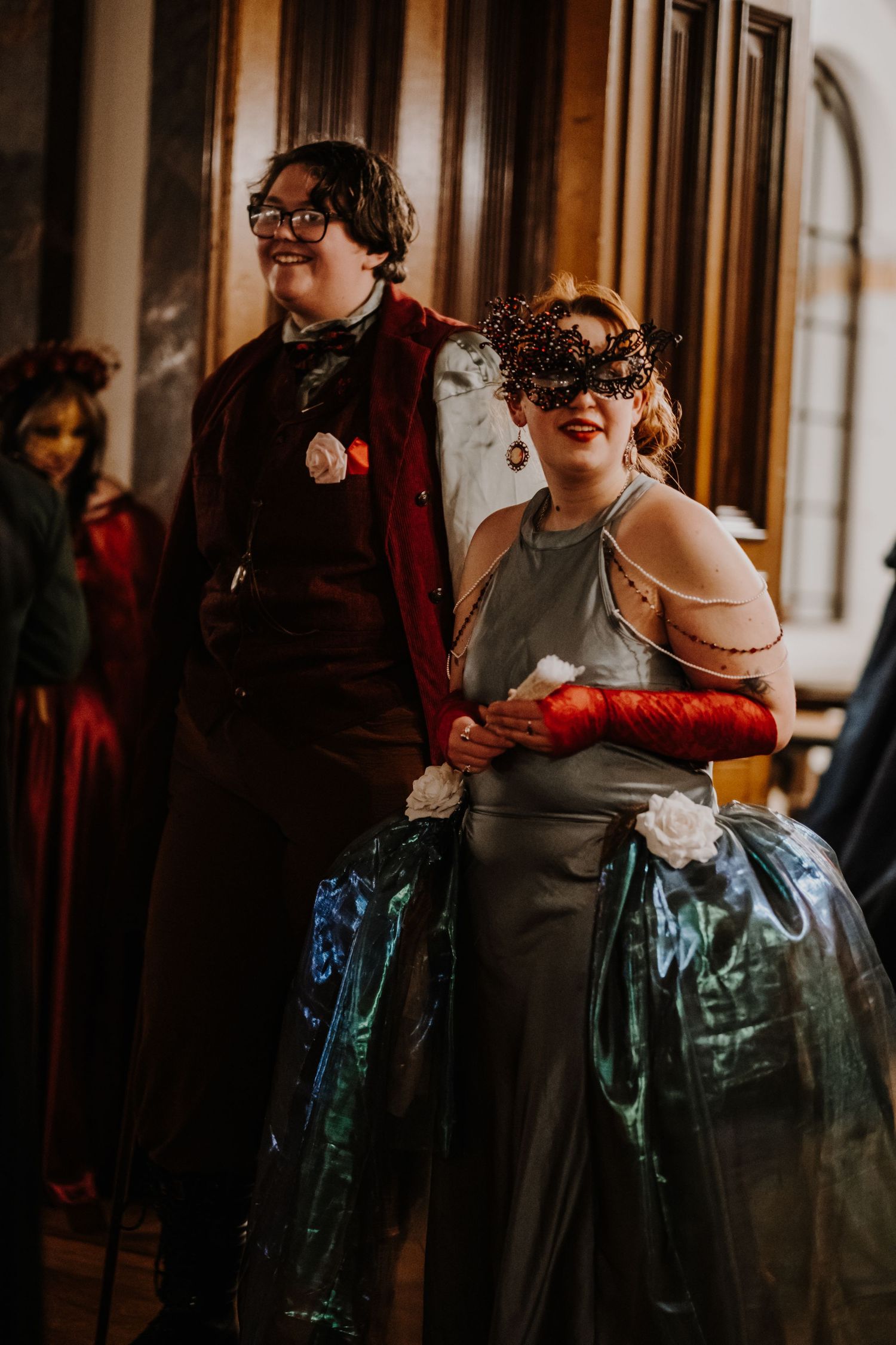 Elegantly dressed couple wearing decorative masks at a formal masquerade event.