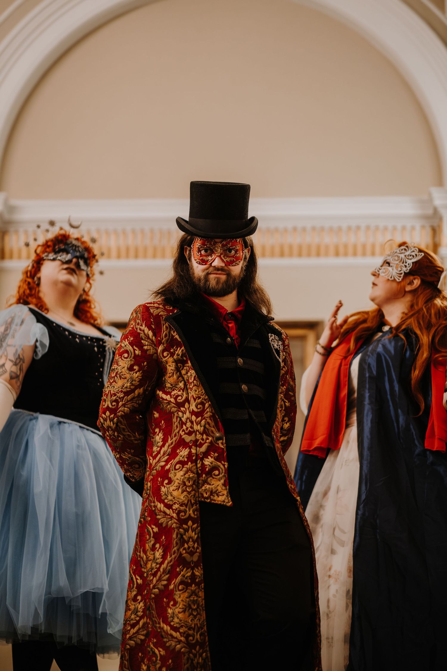 Line of guests in Victorian-inspired costumes and masks at formal masquerade event.