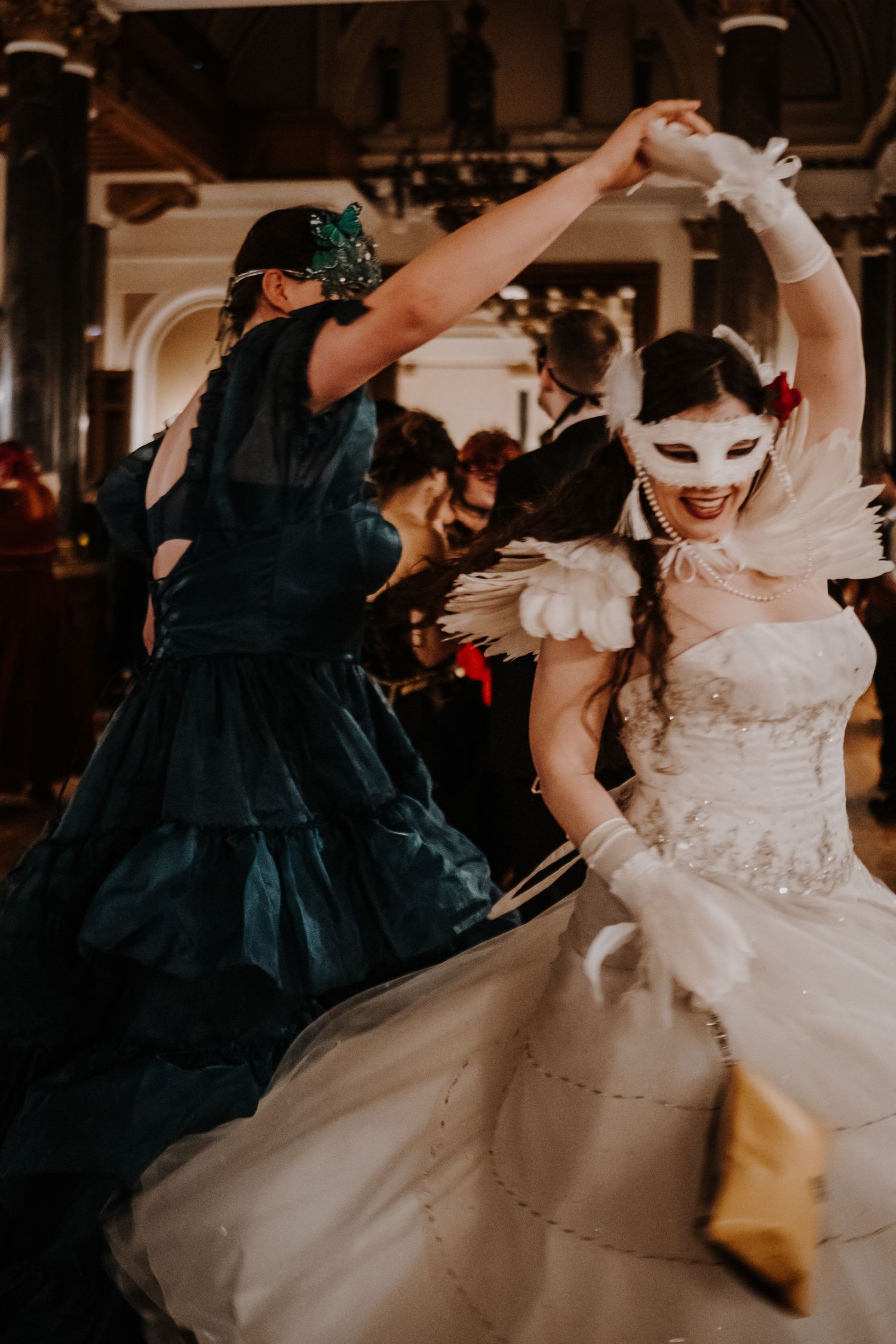 Dancers in white and navy masquerade gowns twirling at formal ball.